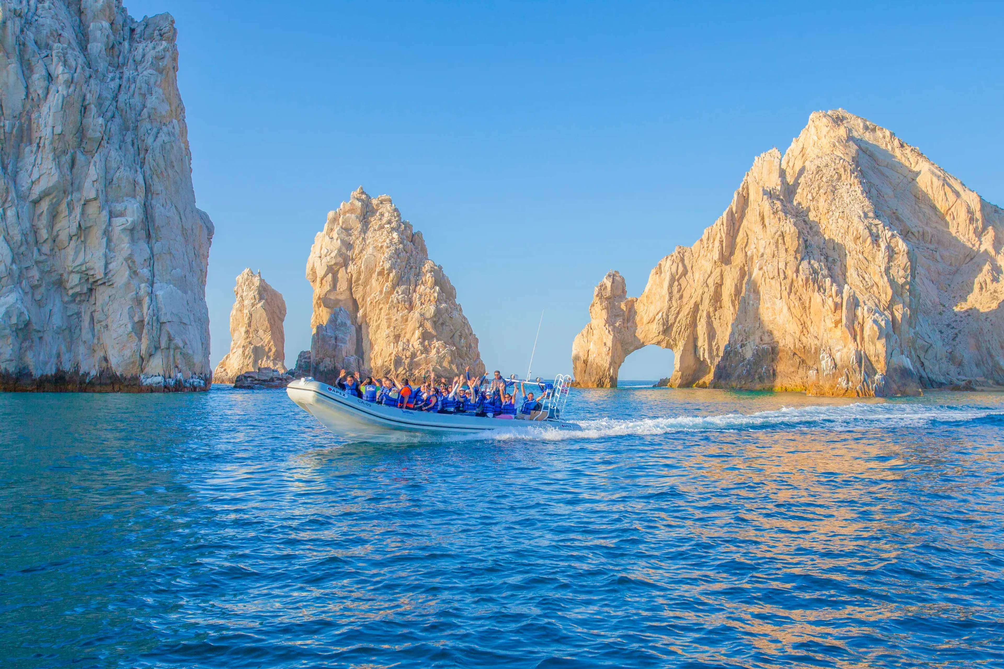 Lancha azul navega por aguas turquesas junto a El Arco, la icónica formación rocosa natural de Cabo San Lucas.