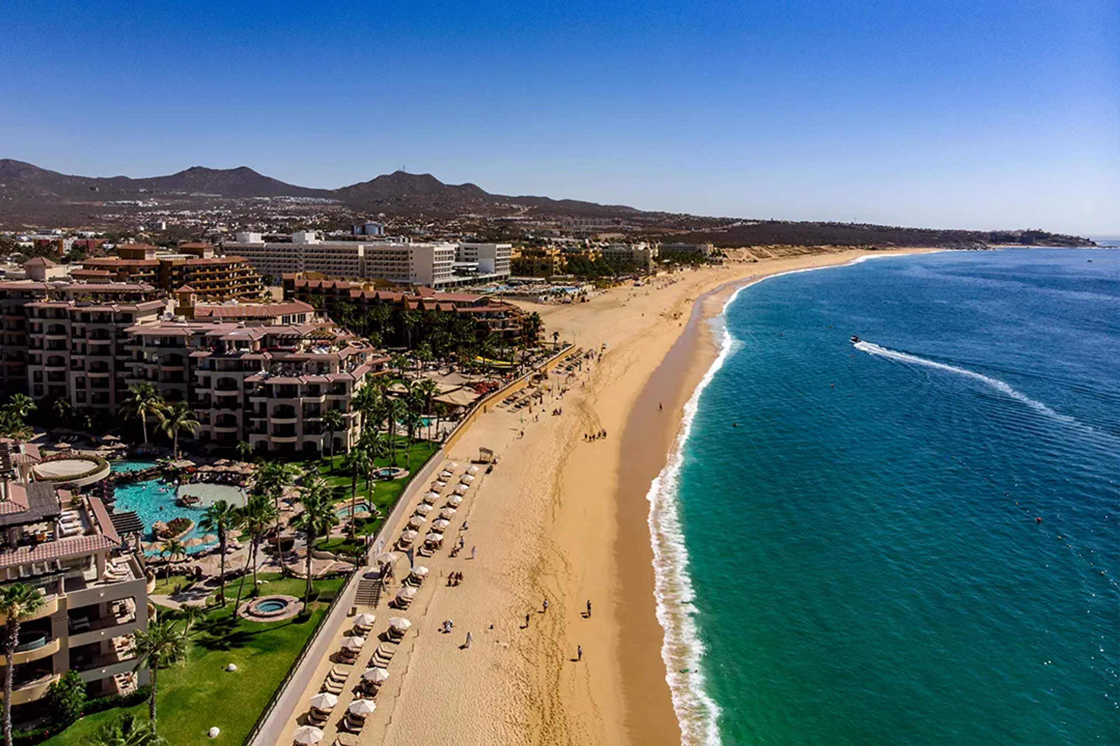 Aerial view of Cabo San Lucas beach with golden sand, luxury resorts, turquoise waters, and coastal scenery
