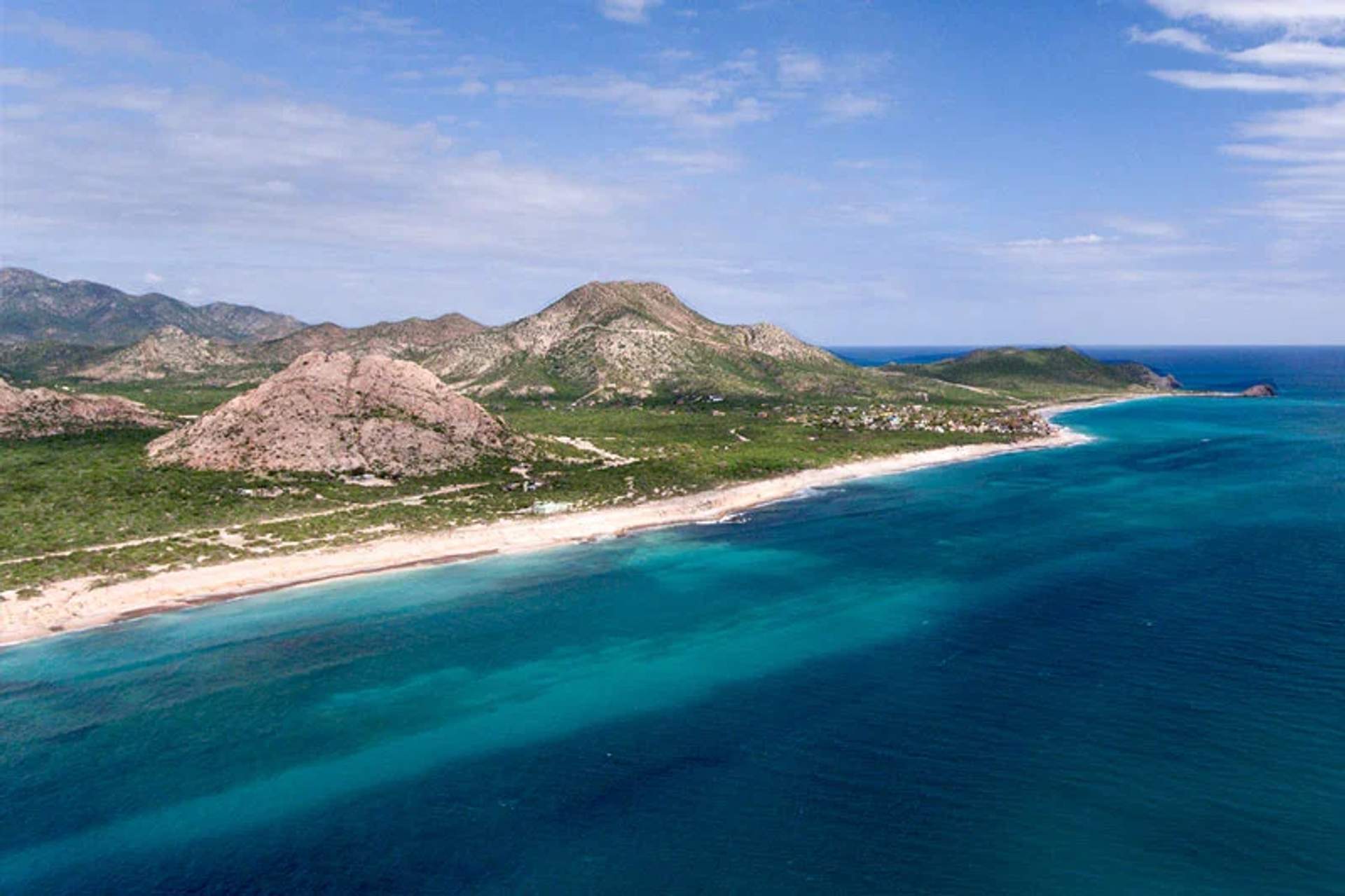 Costa de aguas turquesas y montañas verdes bajo un cielo parcialmente nublado en Cabo Pulmo.