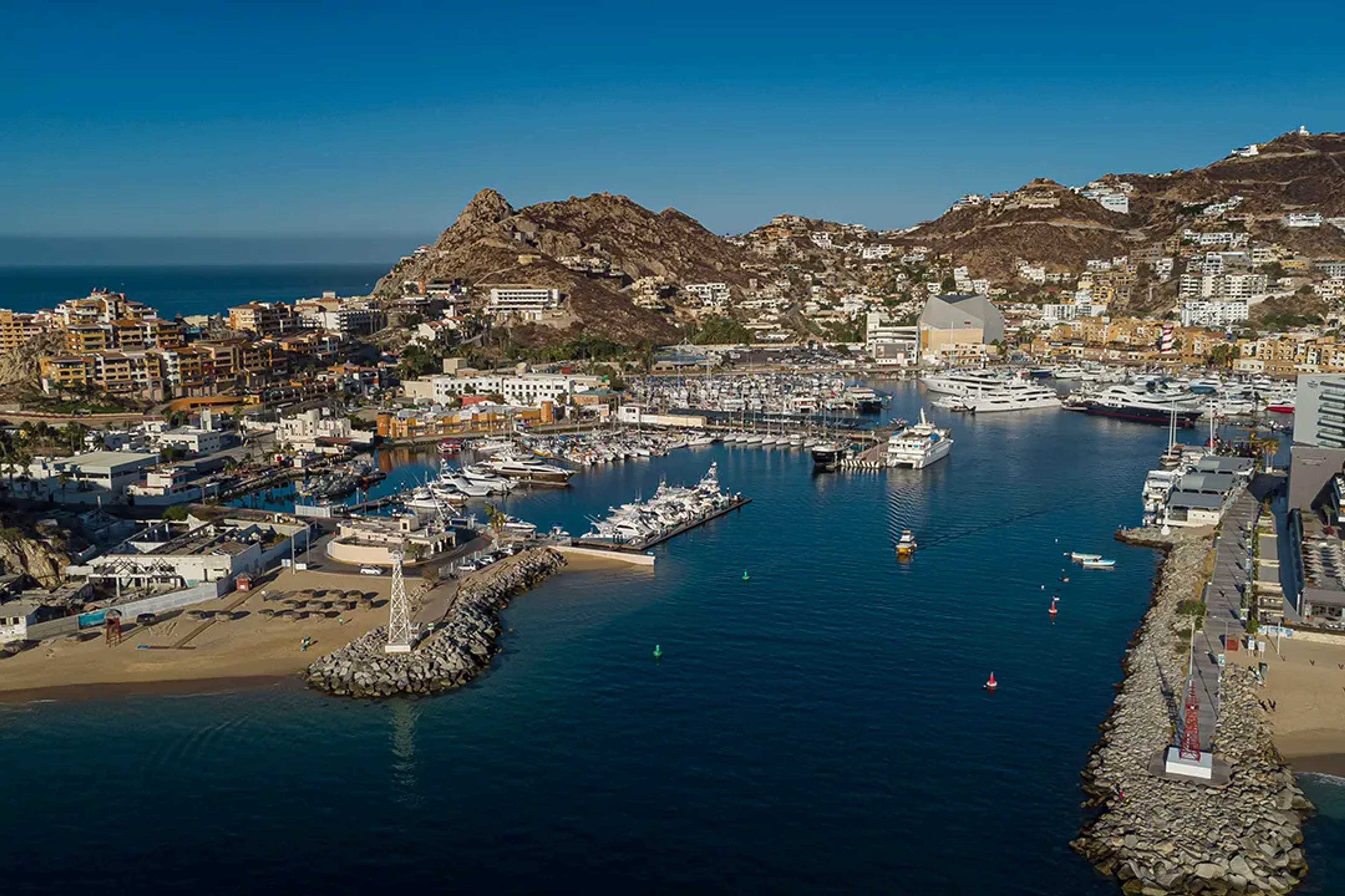Aerial view of Cabo San Lucas Marina, with yachts, beaches, and hills under a clear blue sky.
