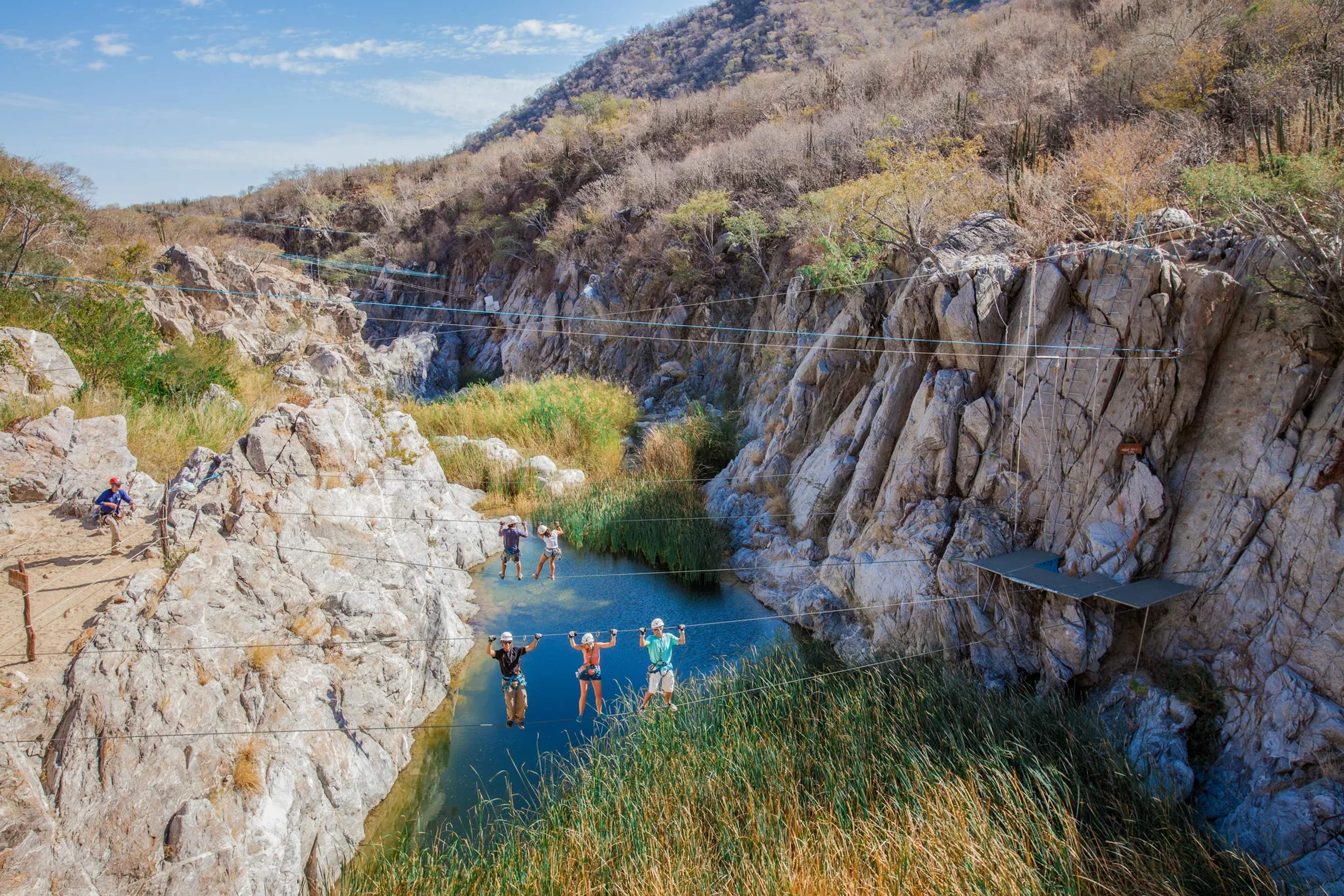 Nadadores disfrutan de las aguas turquesas cristalinas de una cantera rodeada de imponentes acantilados de piedra caliza y vegetación desértica en México.