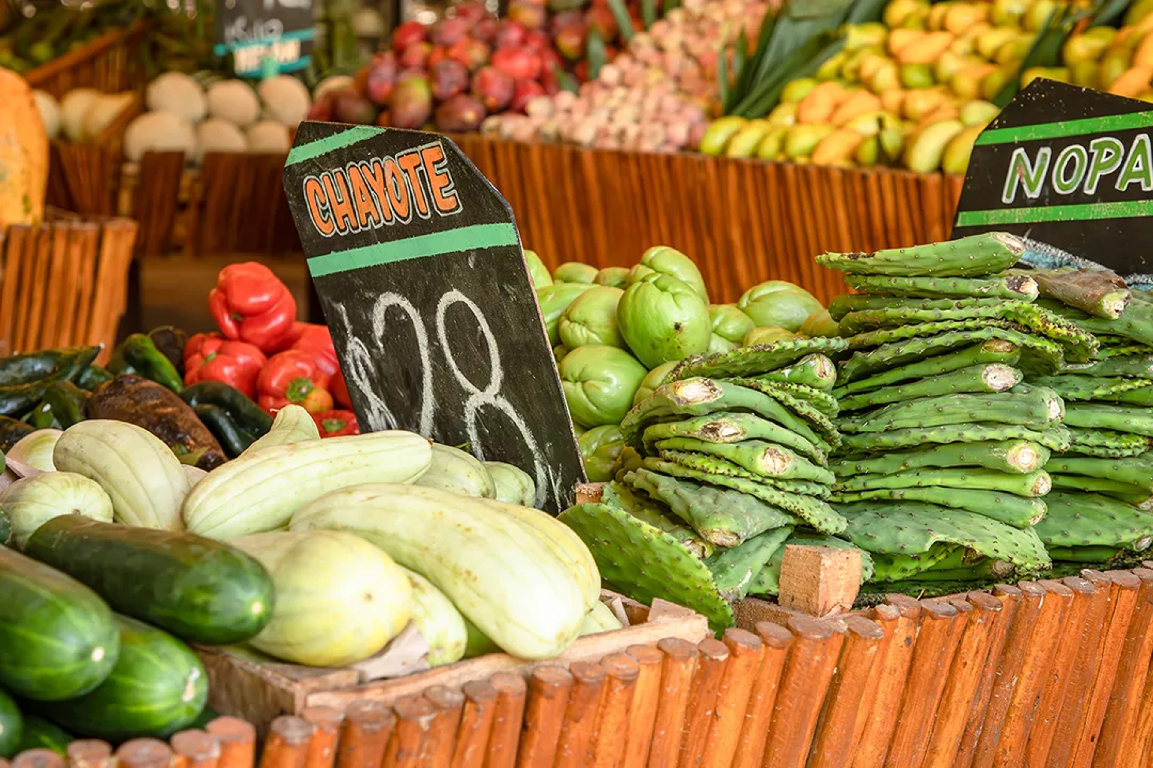 Fresh nopales, chayotes, and vegetables on display at a colorful Mexican market stand.