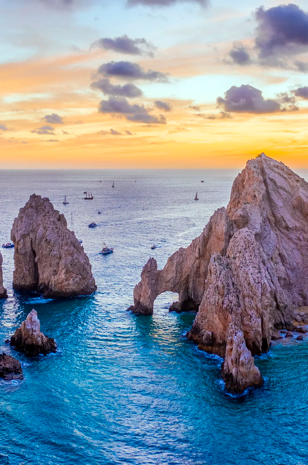 Vista aérea del Arco de Los Cabos con lanchas sobre agua turquesa al atardecer.