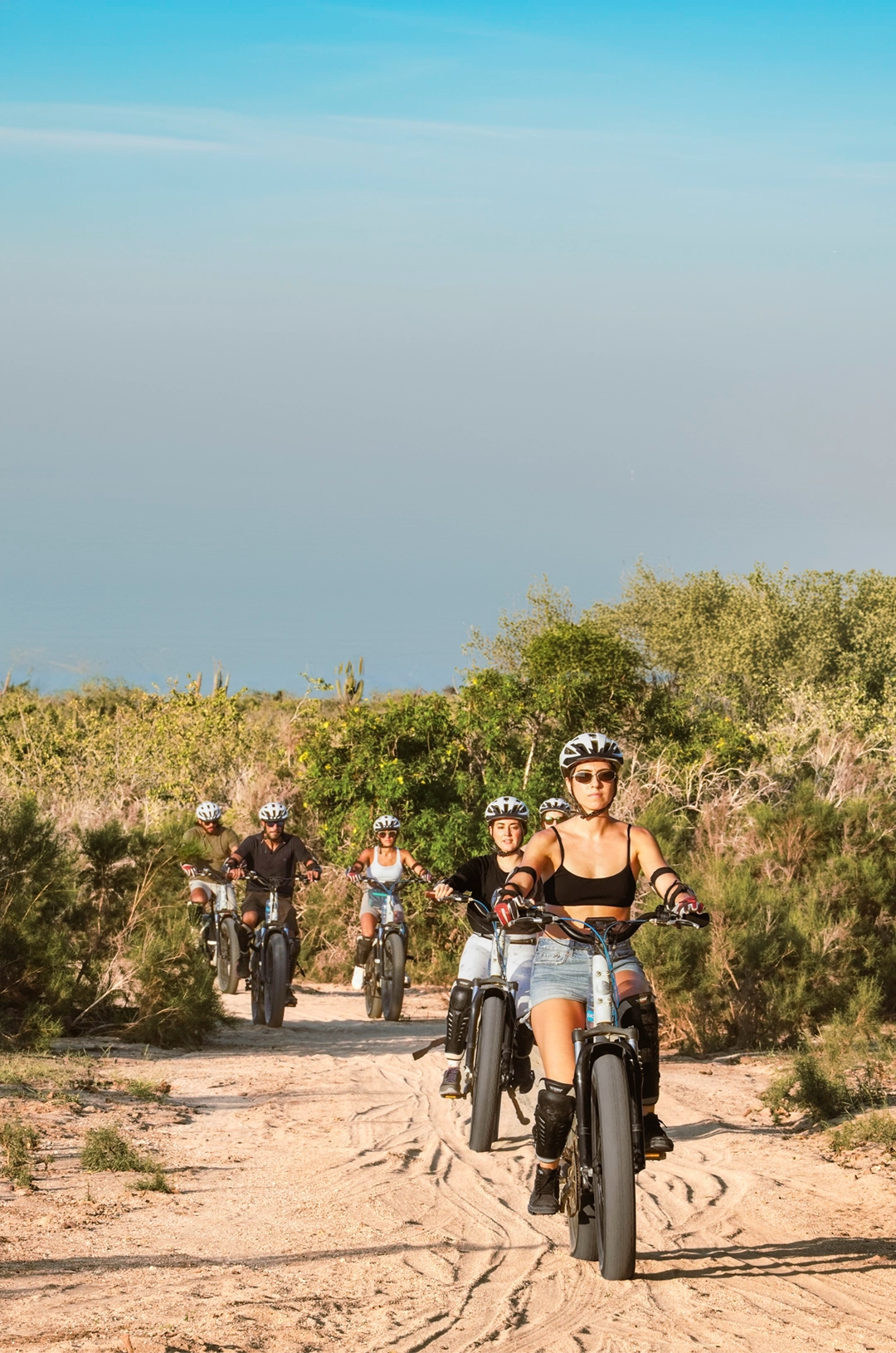 Grupo de ciclistas en bicicletas eléctricas recorriendo senderos naturales bajo un cielo despejado.
