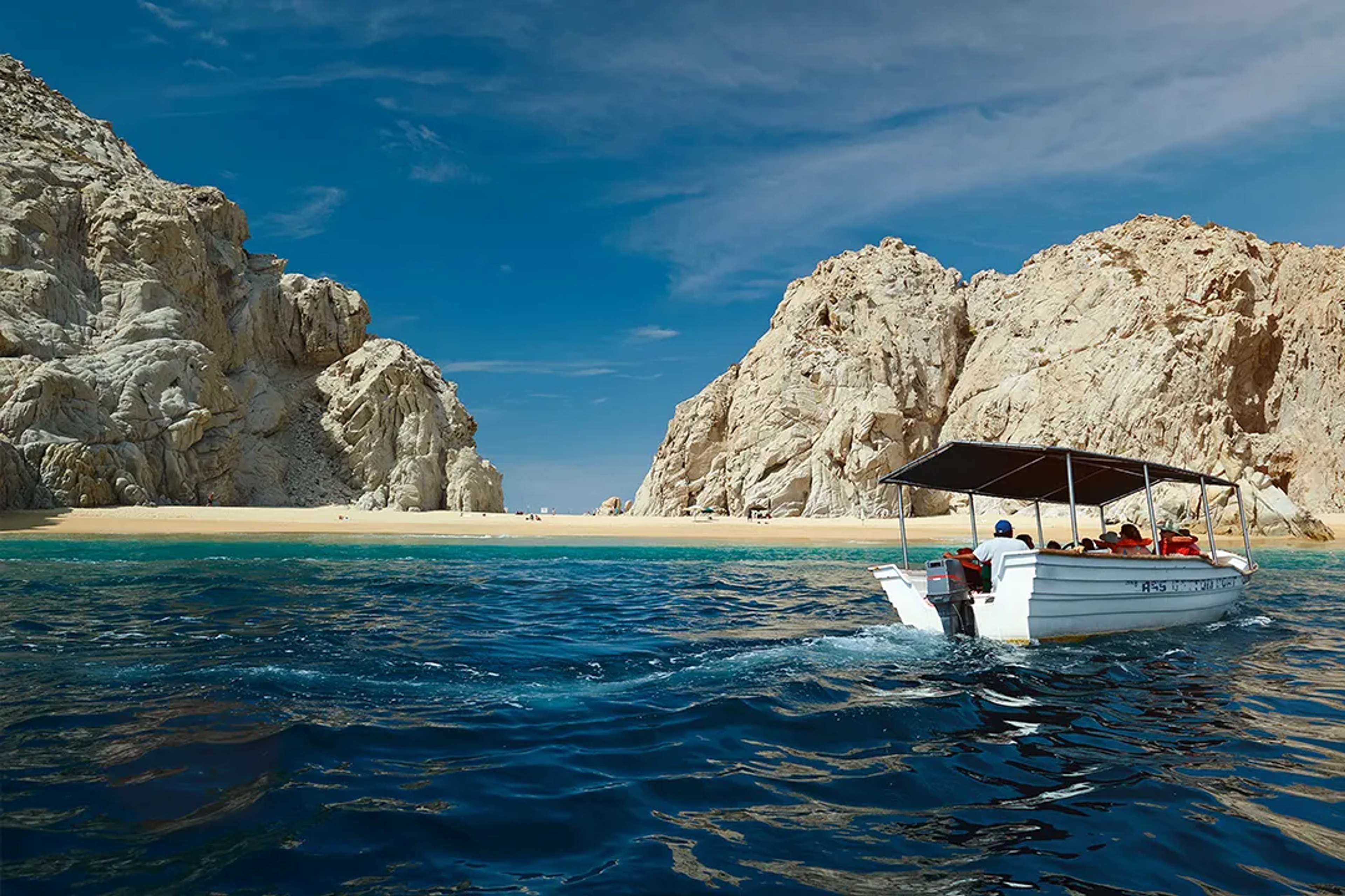 A small boat approaches a golden beach surrounded by dramatic rock formations and deep blue sea.