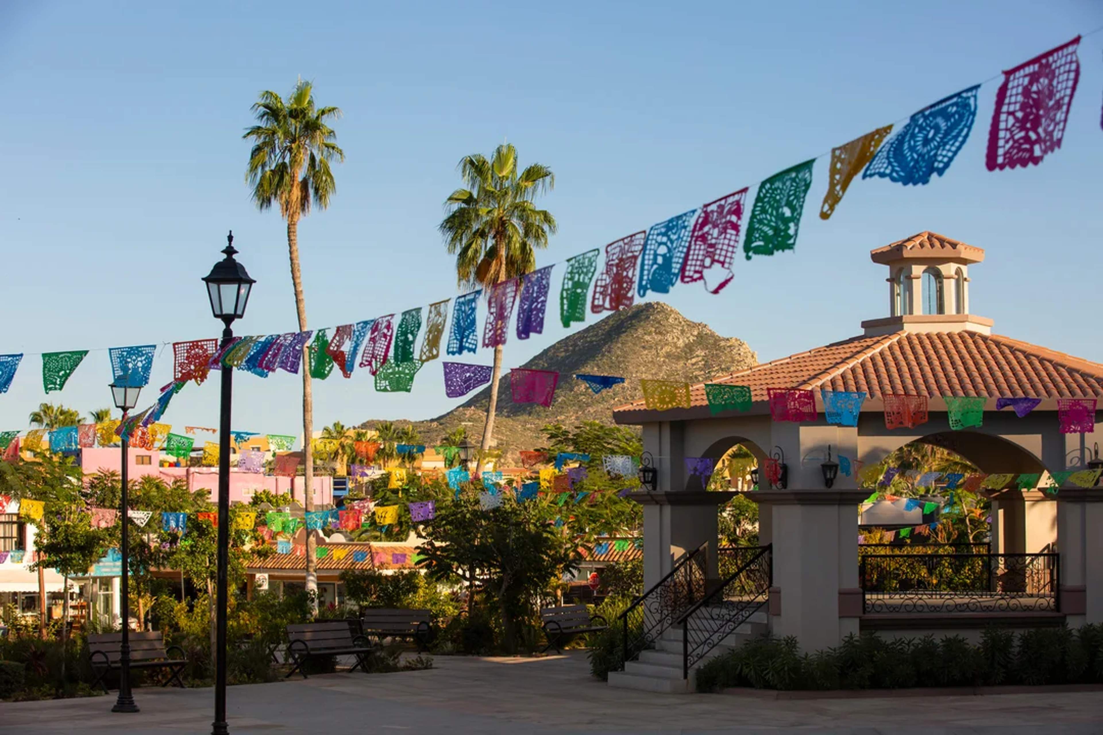 Papel picado decora una encantadora plaza en Cabo, con palmeras y montañas al fondo.