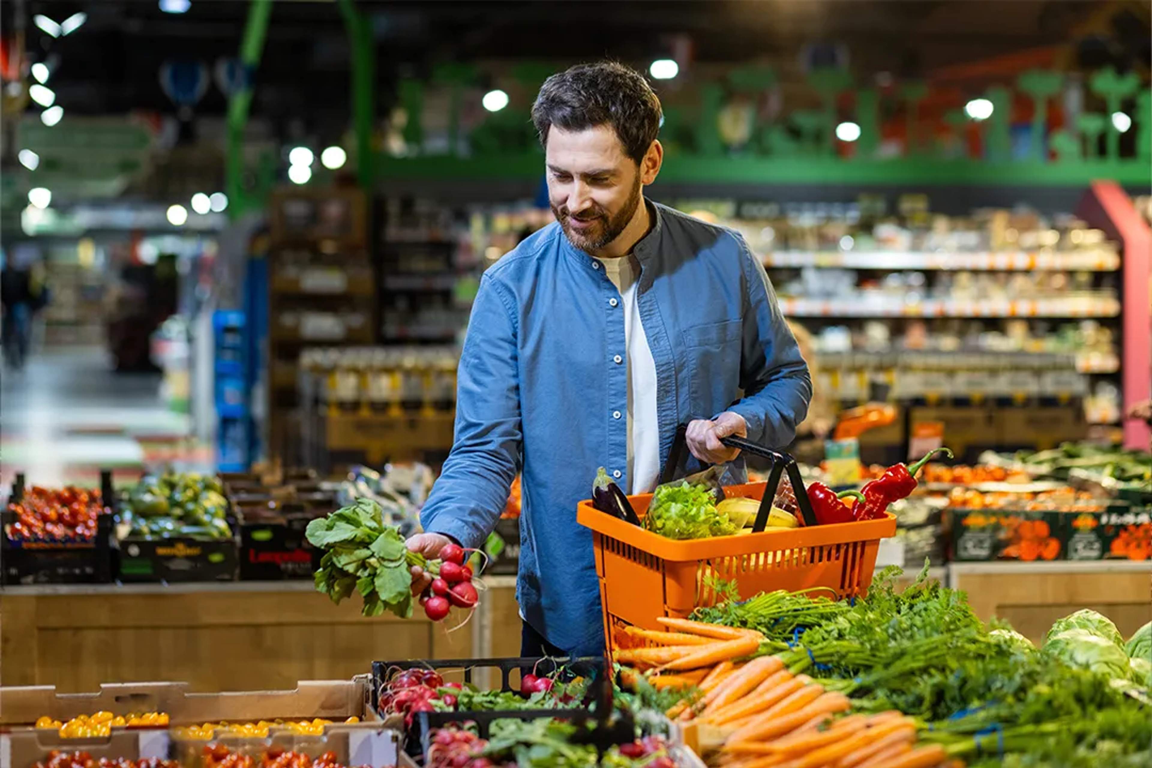 Hombre comprando verduras frescas en un mercado, sostiene rábanos junto a un colorido puesto.