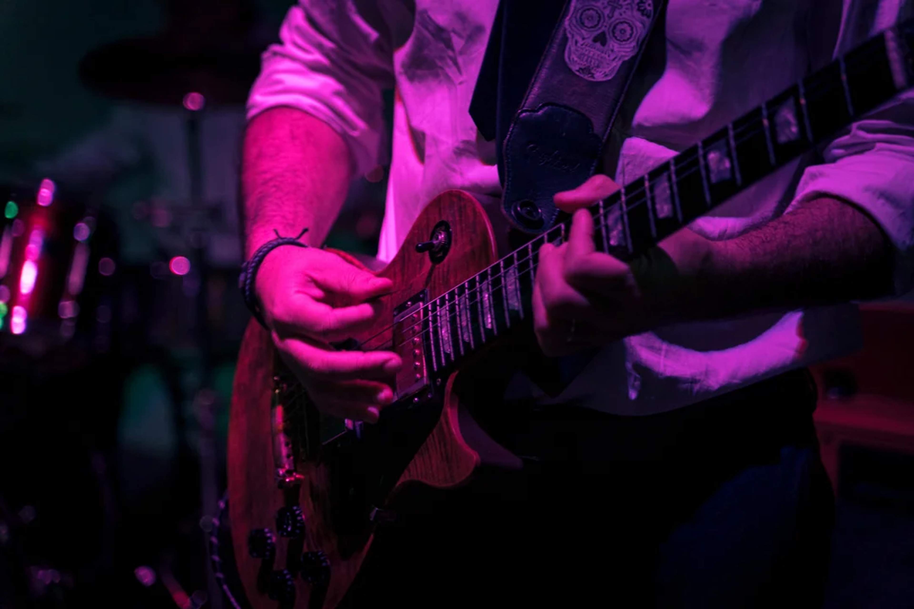 Toma cercana de un guitarrista tocando en vivo bajo luces moradas en una noche musical vibrante.