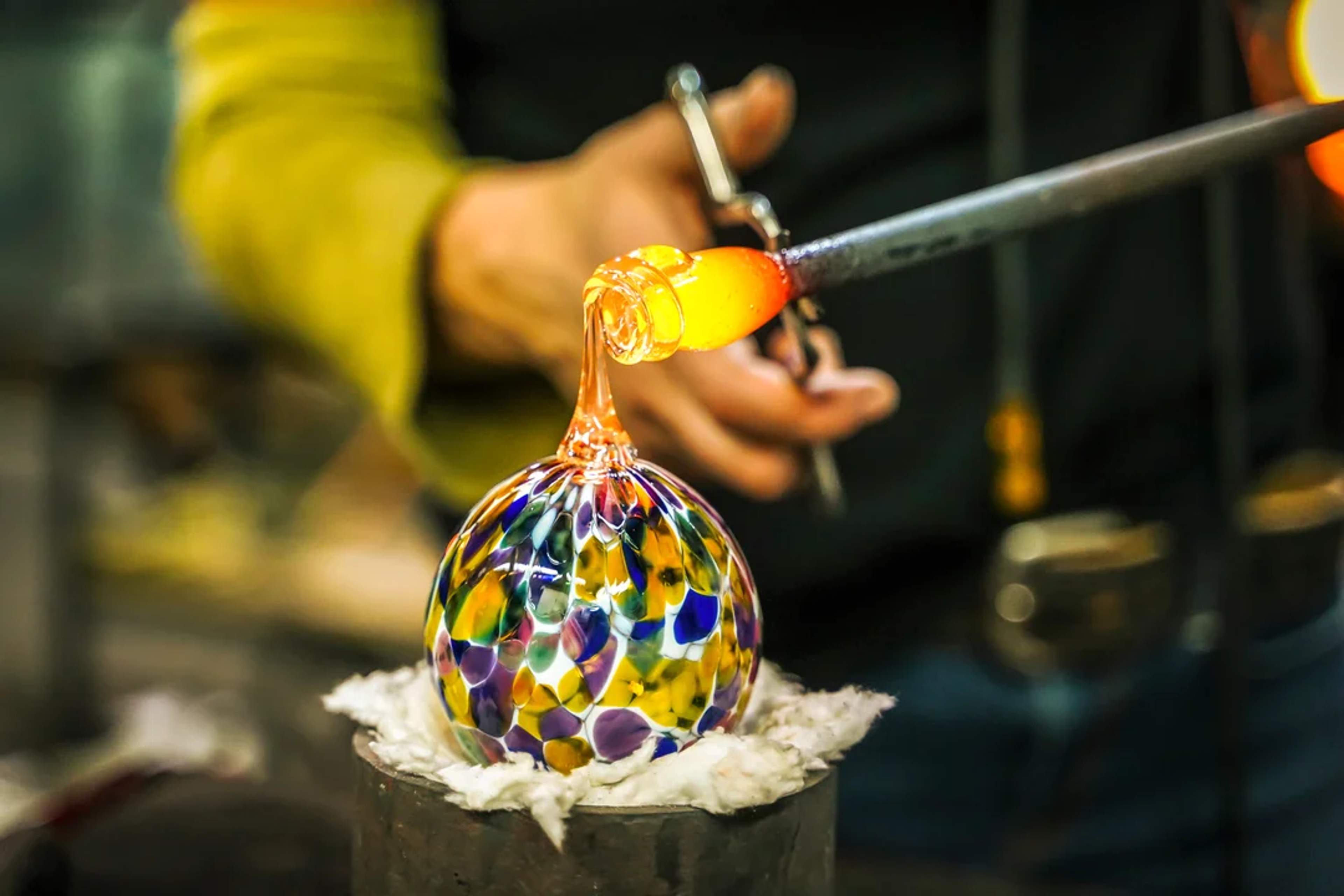 A craftsman shapes a colorful glass sphere with molten glass during a traditional glassblowing.