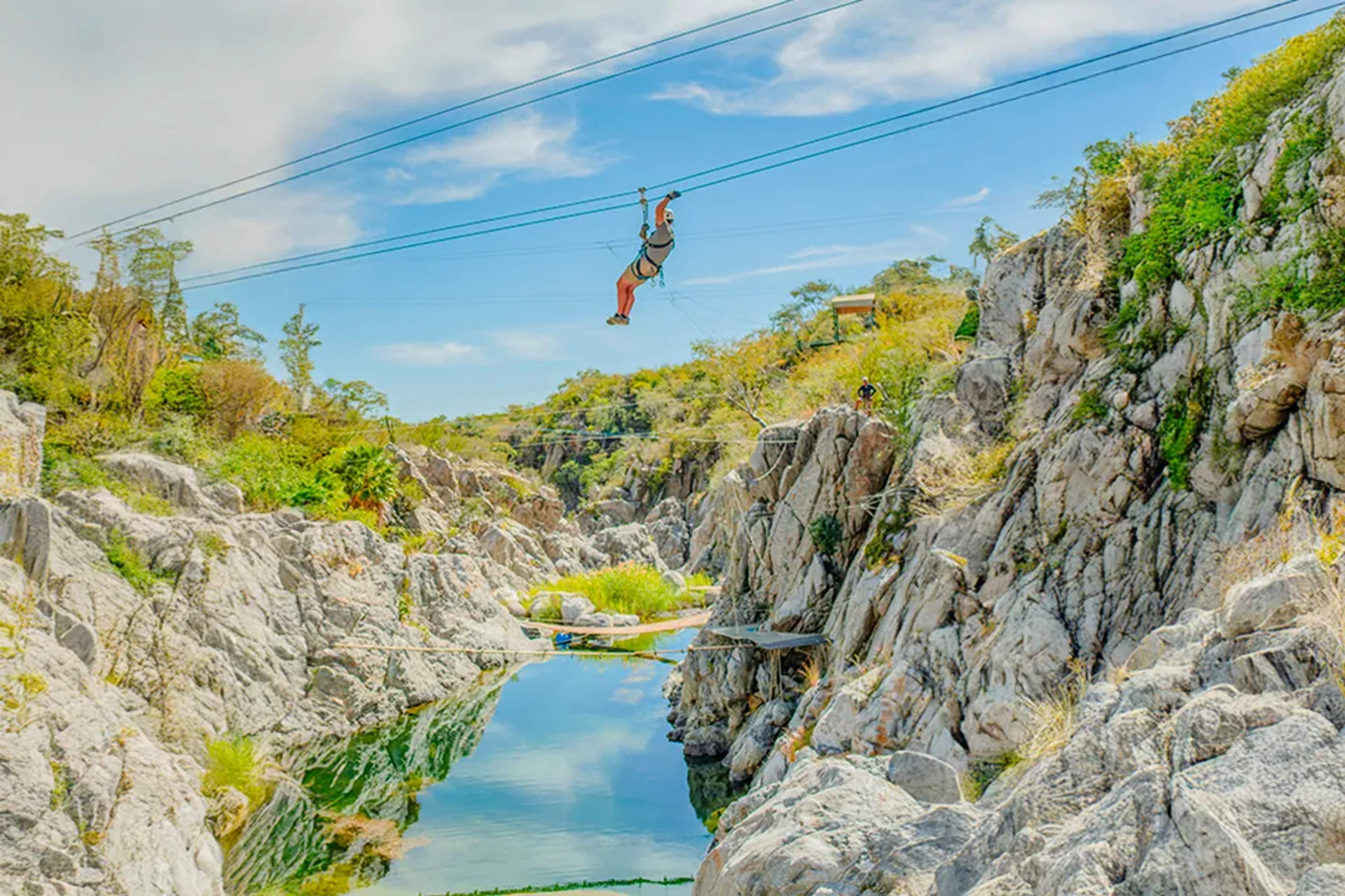 Ziplining over desert canyon in Los Cabos with rocky cliffs, river below, and outdoor adventure setting