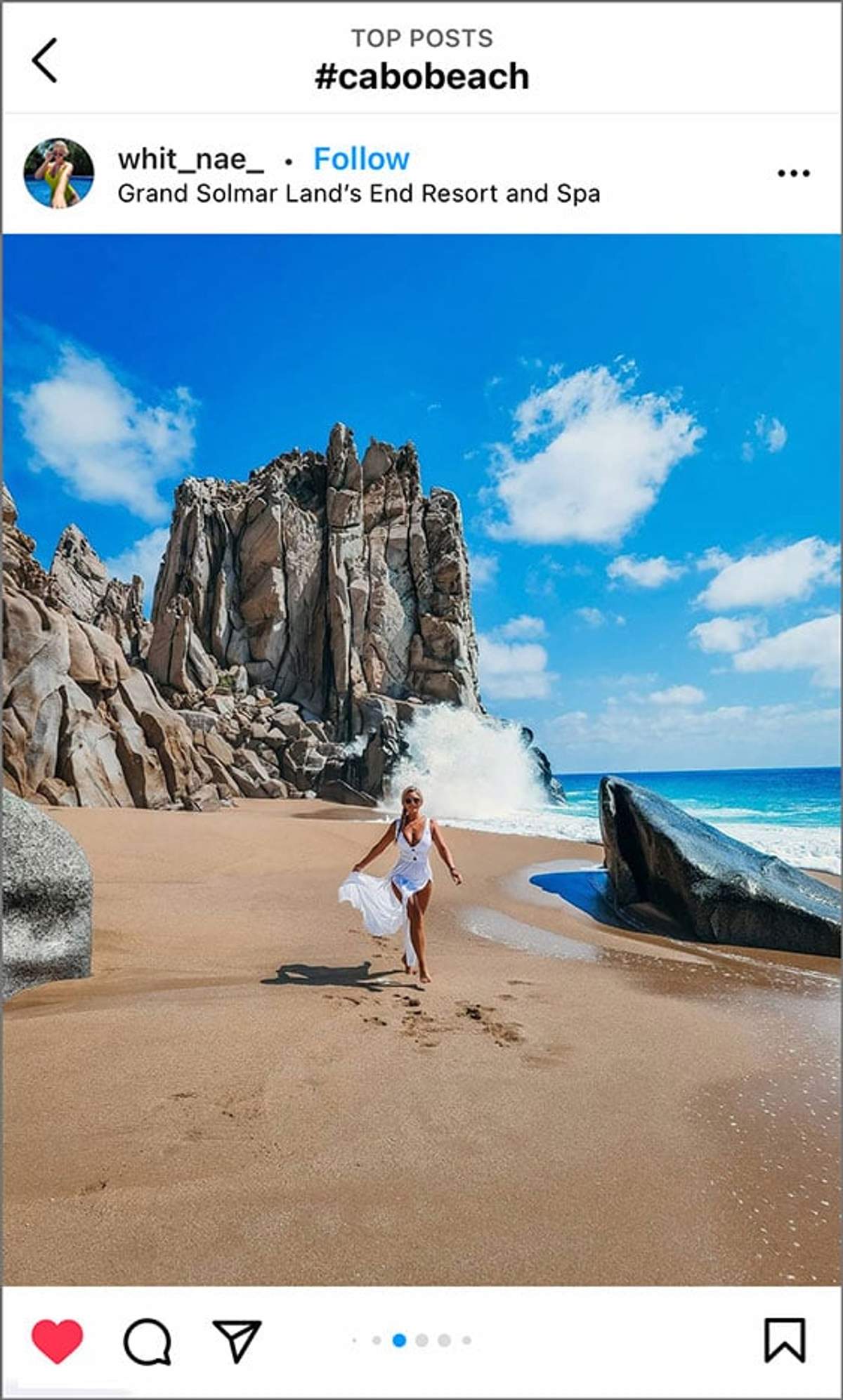Mujer con vestido blanco corriendo en una playa de arena con acantilados rocosos y olas rompiendo en Grand Solmar Land's End Resort.