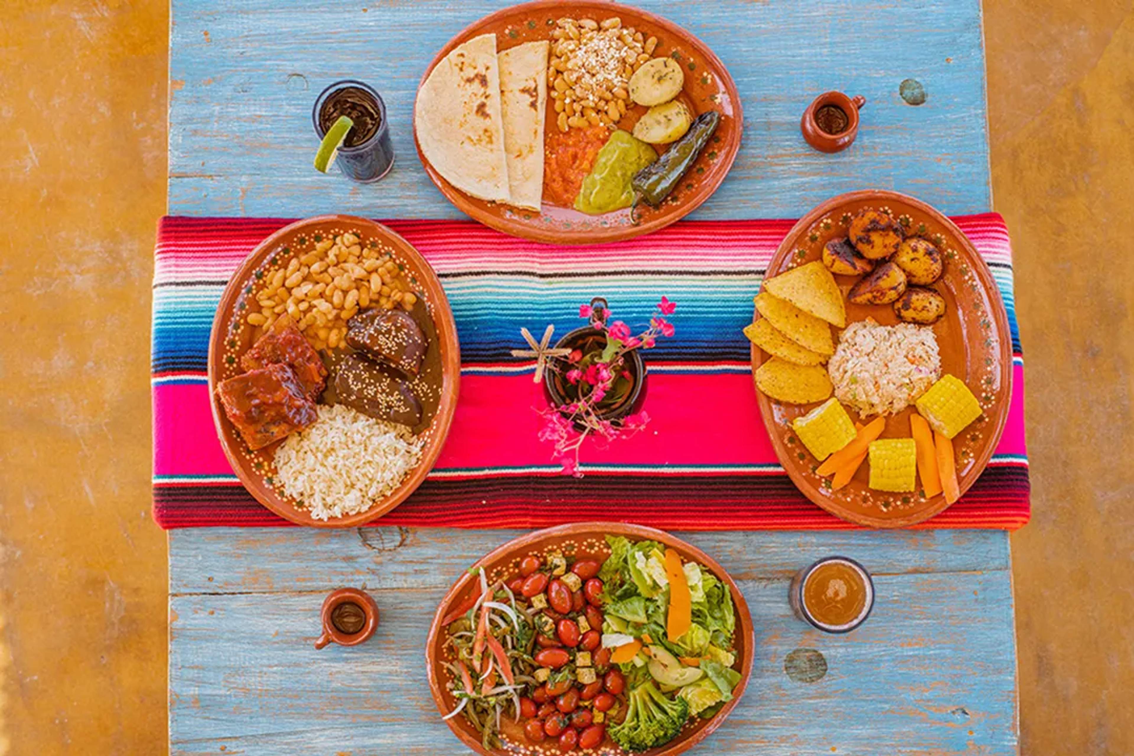 Colorful table with traditional Mexican dishes, rice, mole, tortillas, and fresh salad.