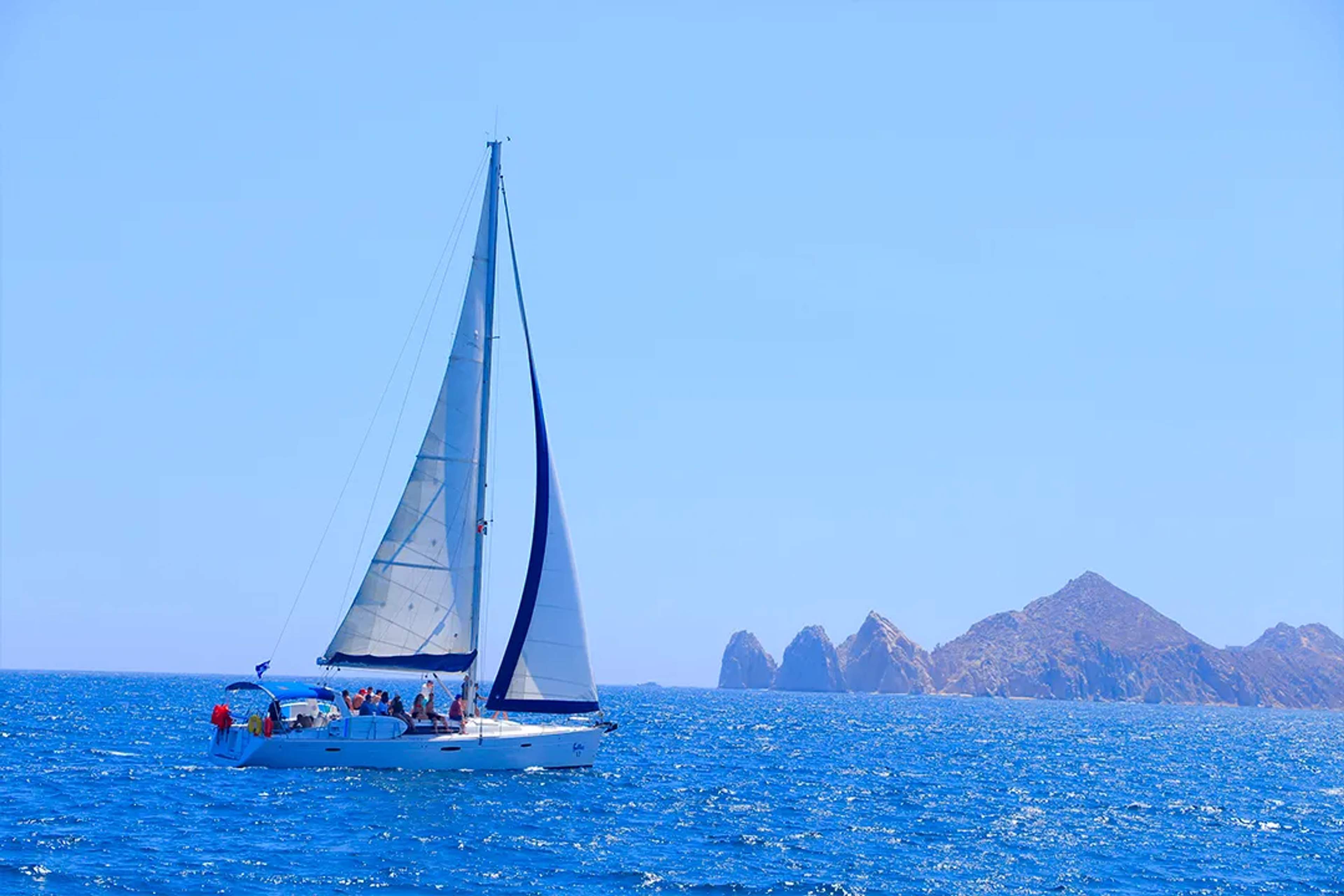 Catamarán navegando en el Mar de Cortés frente a Cabo San Lucas, con cielo despejado, mar azul intenso y formaciones rocosas icónicas