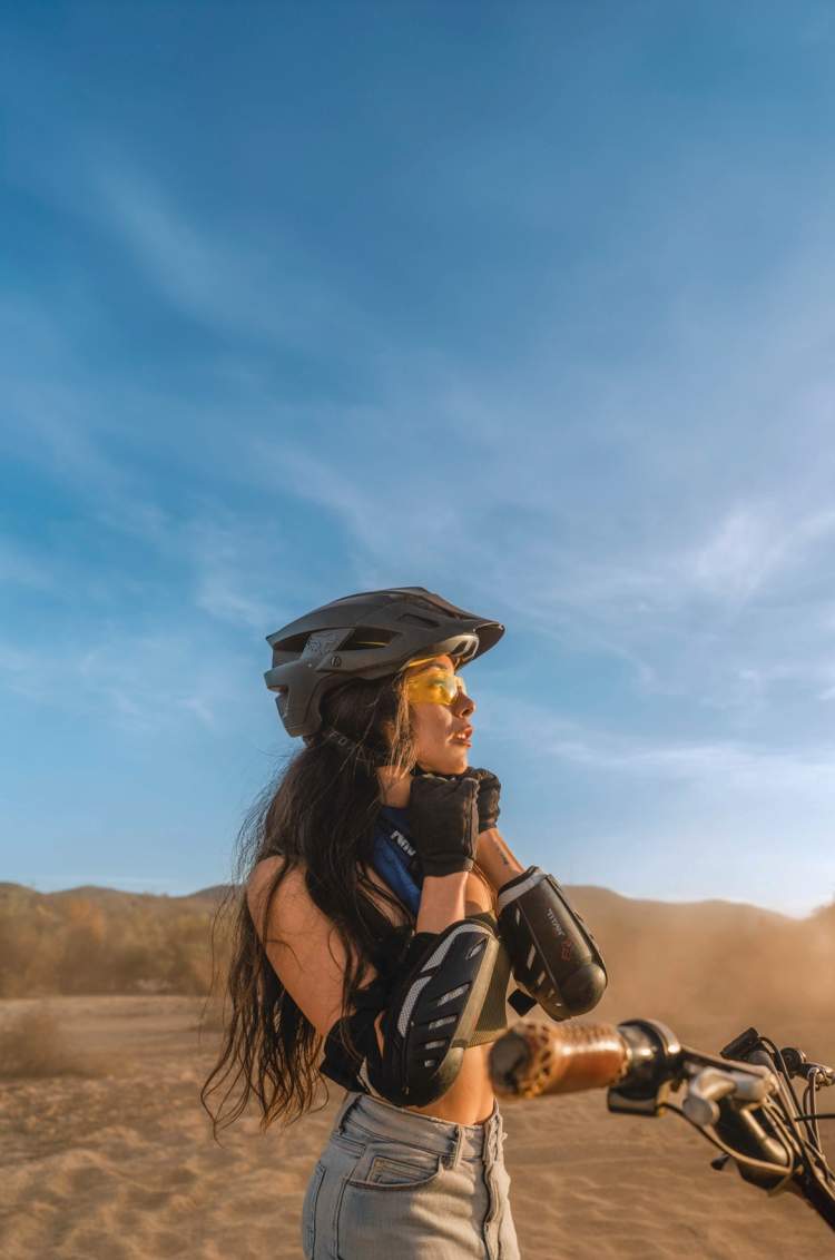Woman adjusting her helmet in a sandy desert landscape.