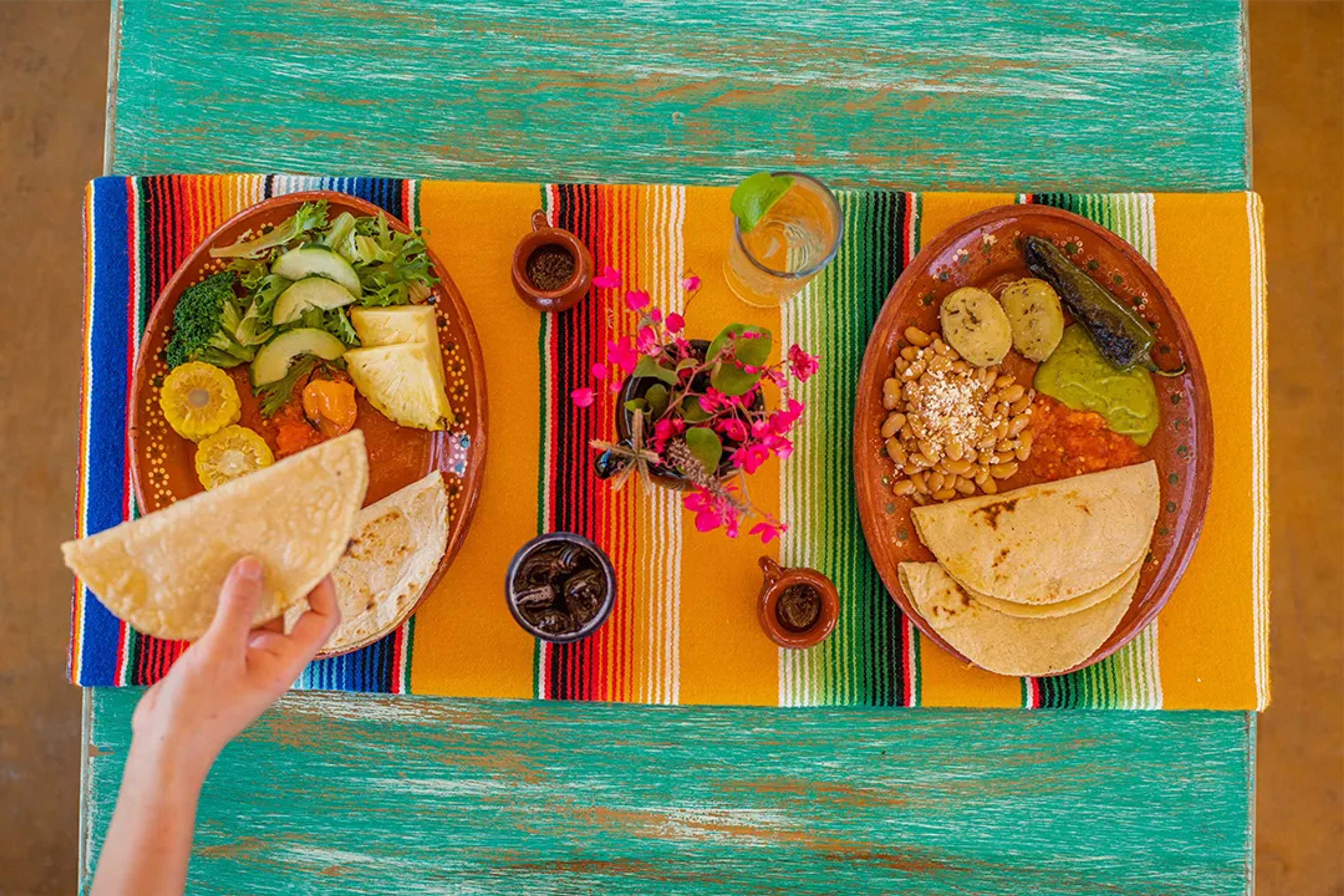 Traditional Mexican dishes with tortillas, salad, beans, and salsa on a colorful tablecloth.