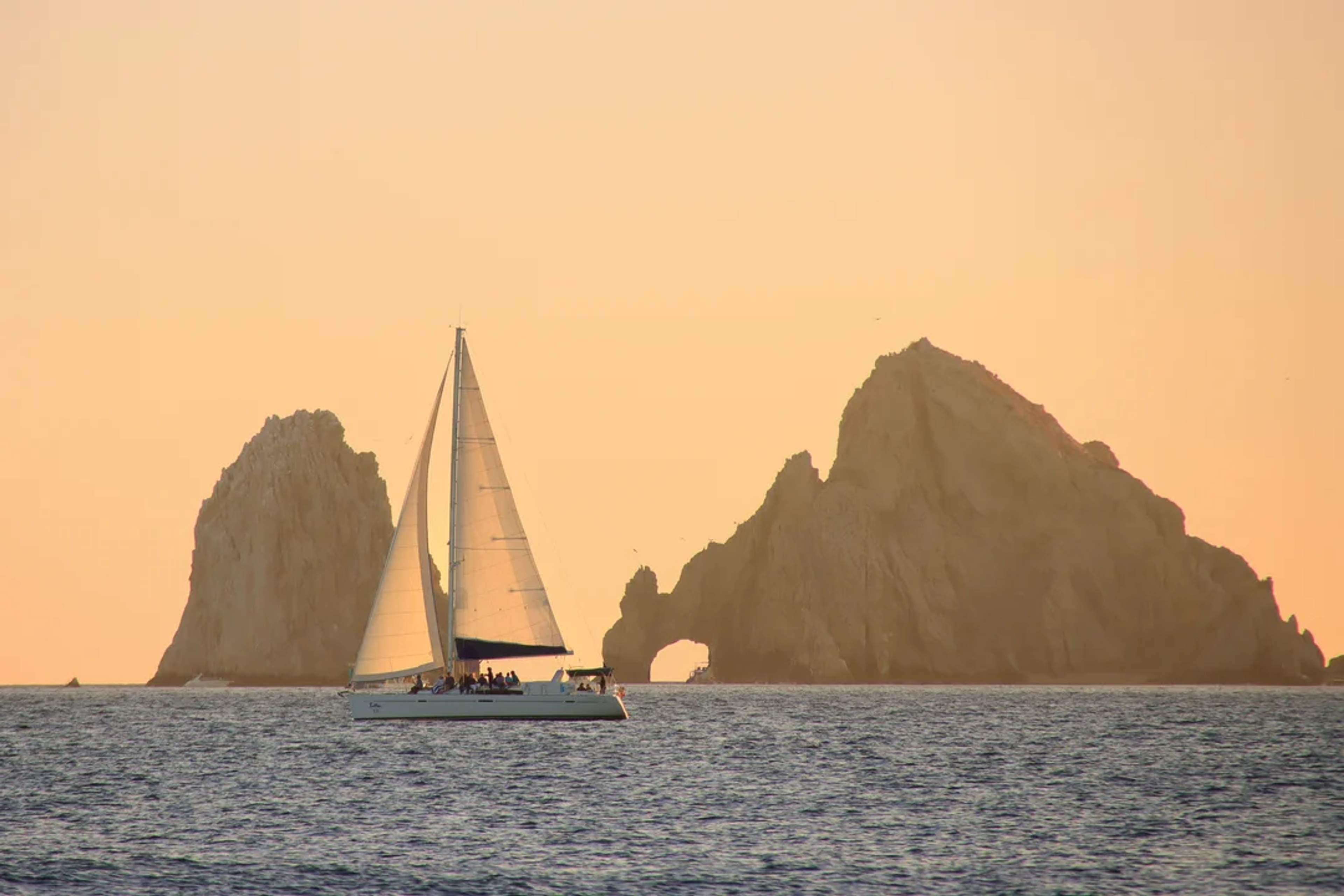 Sailboat glides by the Arch of Cabo San Lucas at sunset, creating a peaceful ocean scene.
