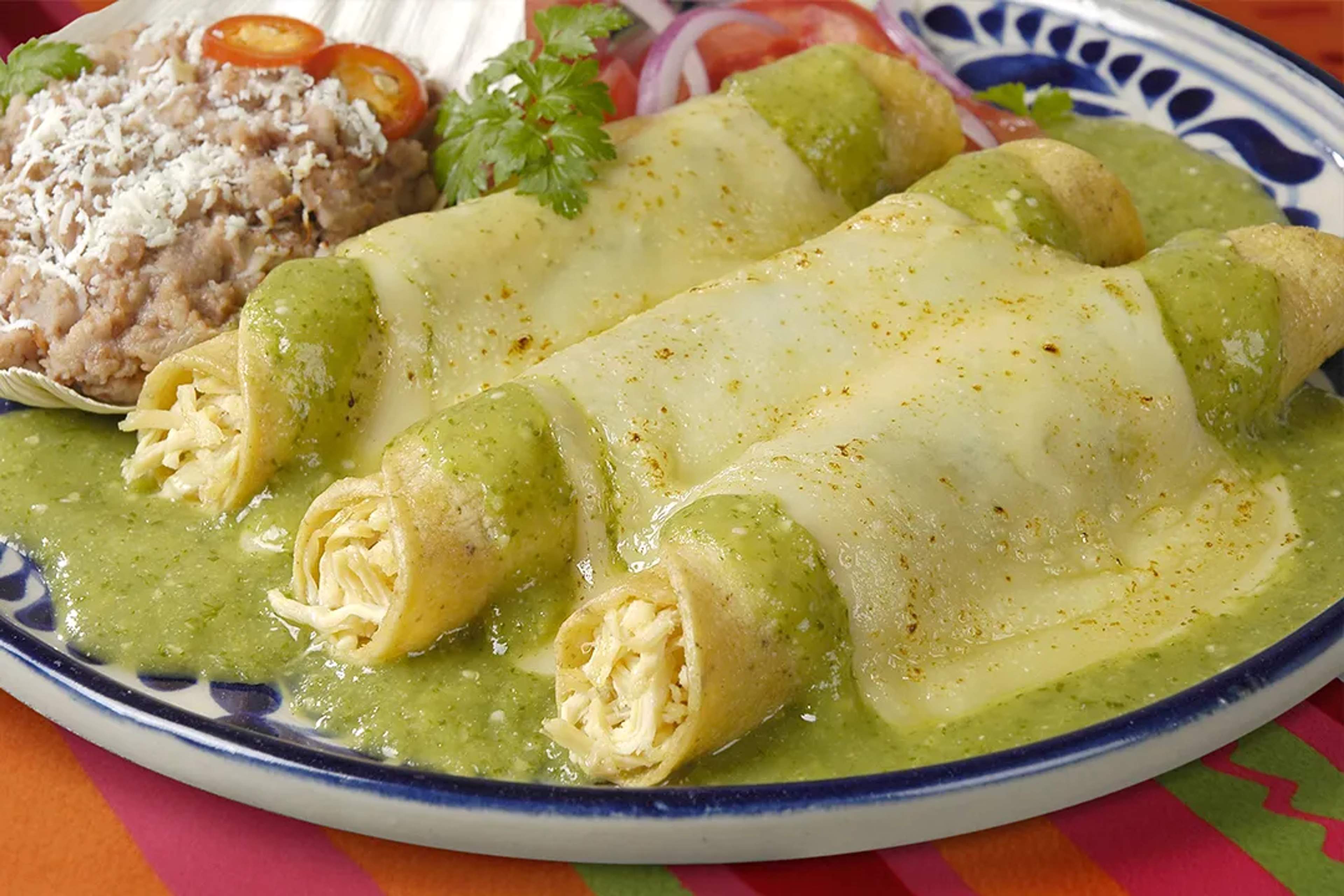 Enchiladas de queso con salsa verde, cubiertas de queso derretido y frijoles refritos.