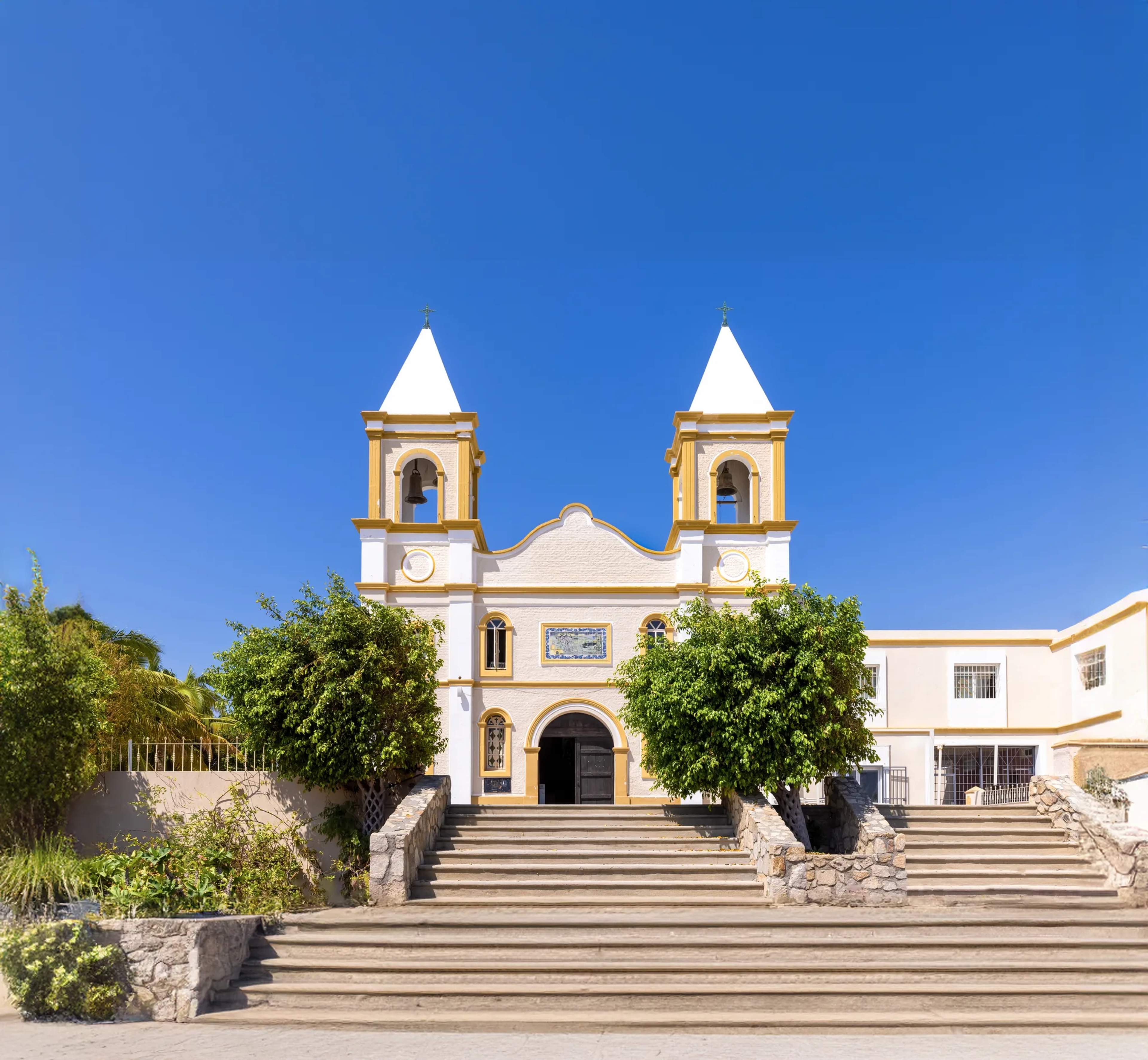 Iglesia colonial de muros blancos y chapiteles dorados brillando al sol en la plaza principal de San José del Cabo