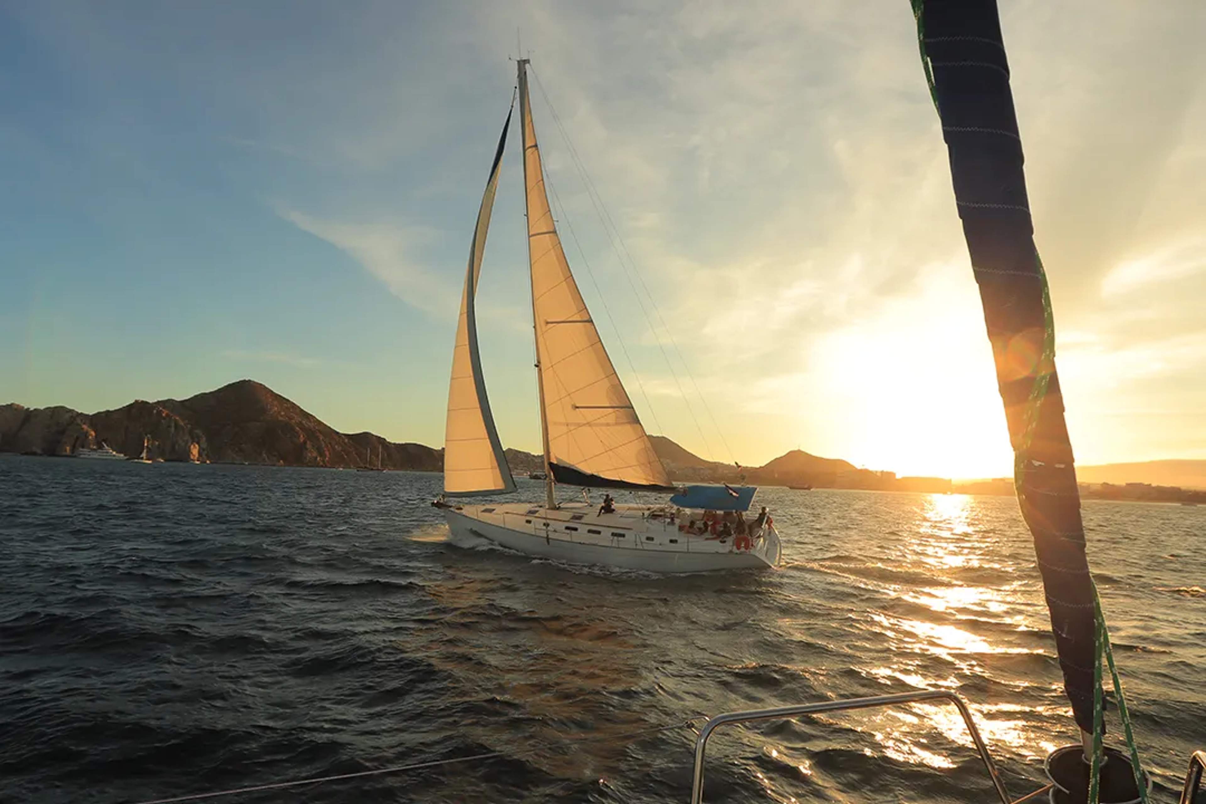 Velero de lujo navegando al atardecer en Cabo San Lucas con cielo dorado y tour escénico por Mar de Cortés MX.