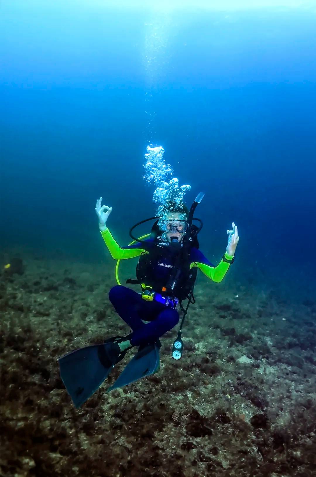 Buzo submarino haciendo la señal de "OK" con la mano, con burbujas ascendiendo en el océano azul profundo.