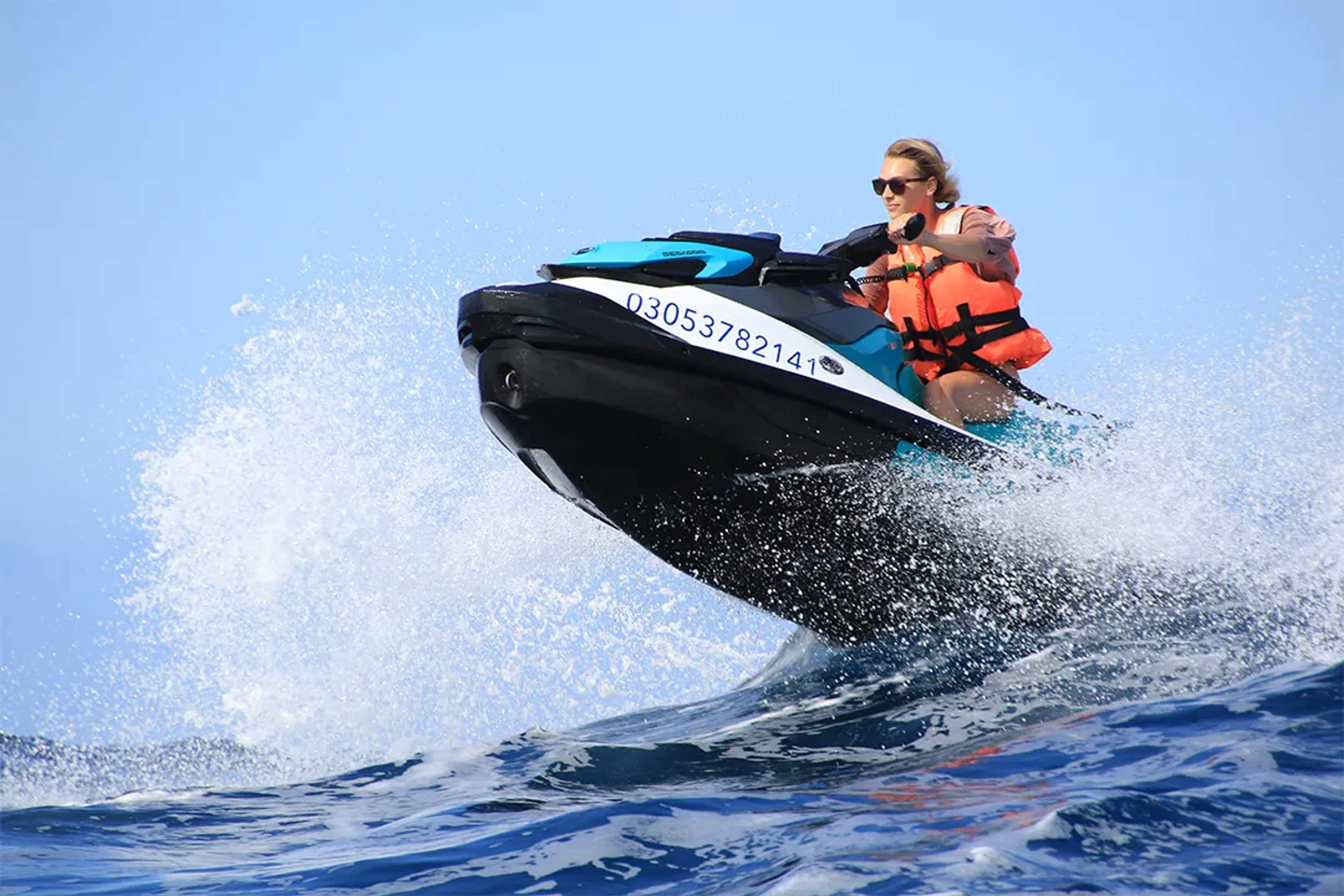 Mujer conduce una moto acuática sobre las olas, con chaleco salvavidas y gafas de sol.