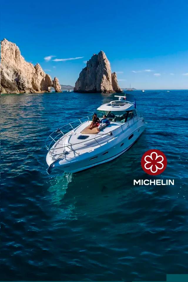  A luxury yacht cruises near the iconic rock formations of Los Cabos under a clear blue sky, with two people relaxing on deck