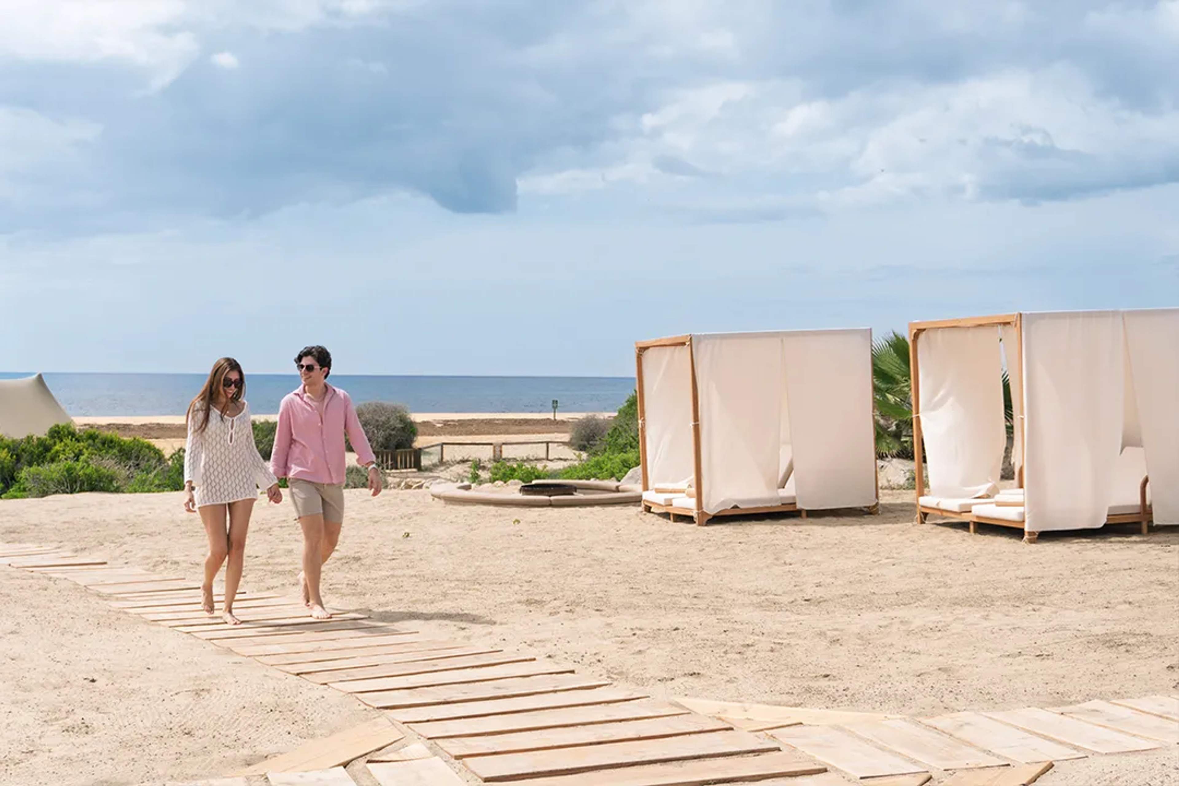 Couple walking hand in hand at a luxury beach club in Los Cabos, enjoying a relaxed and romantic seaside day