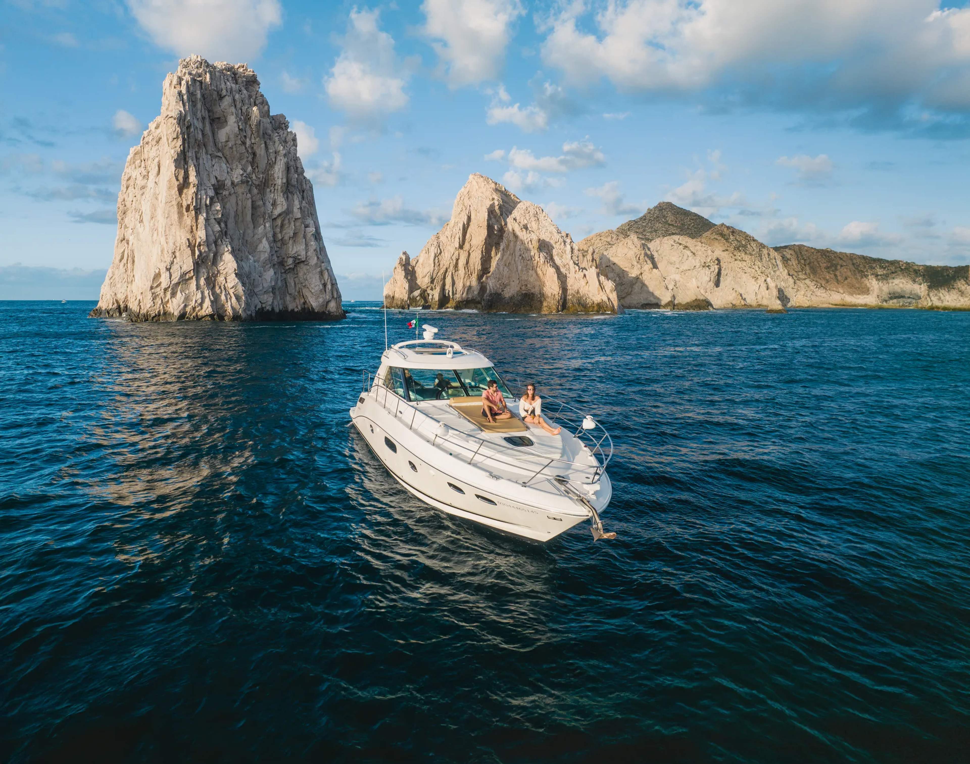 A white luxury yacht anchors in turquoise waters near dramatic rocky cliffs and coastline in Cabo San Lucas, Mexico.