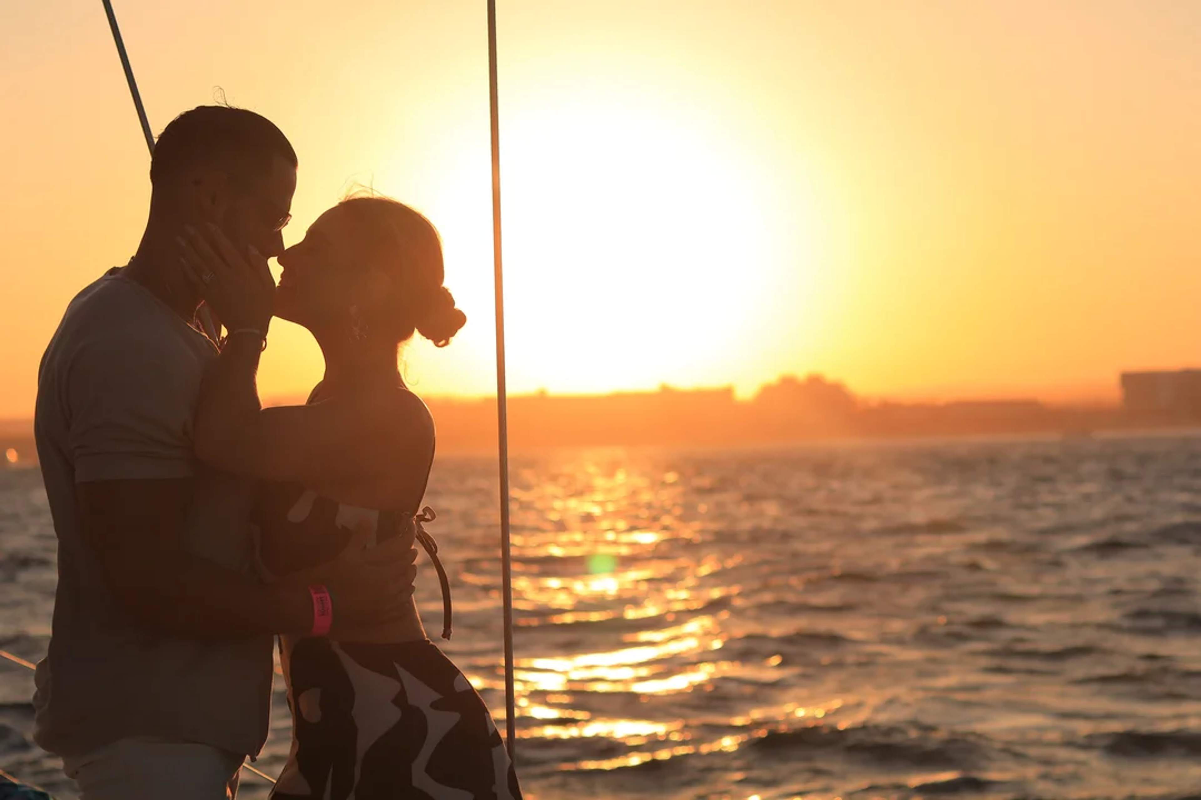 Pareja se besa al atardecer en un velero, envueltos en la luz dorada del océano.