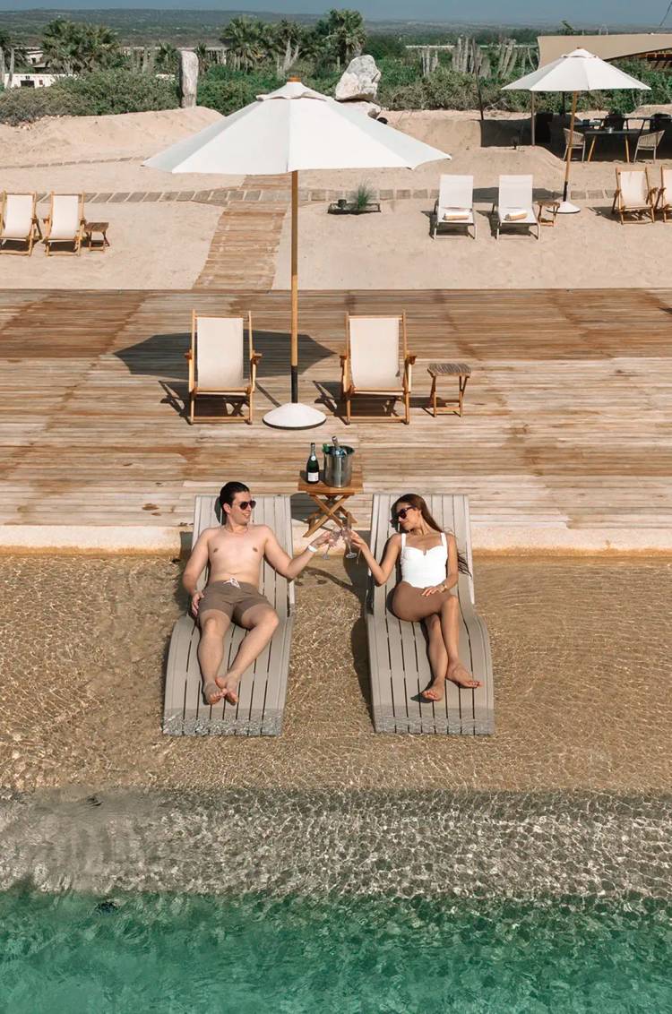 Couple relaxing on loungers with champagne at Tierra Sagrada Beach Club in Cabo San Lucas