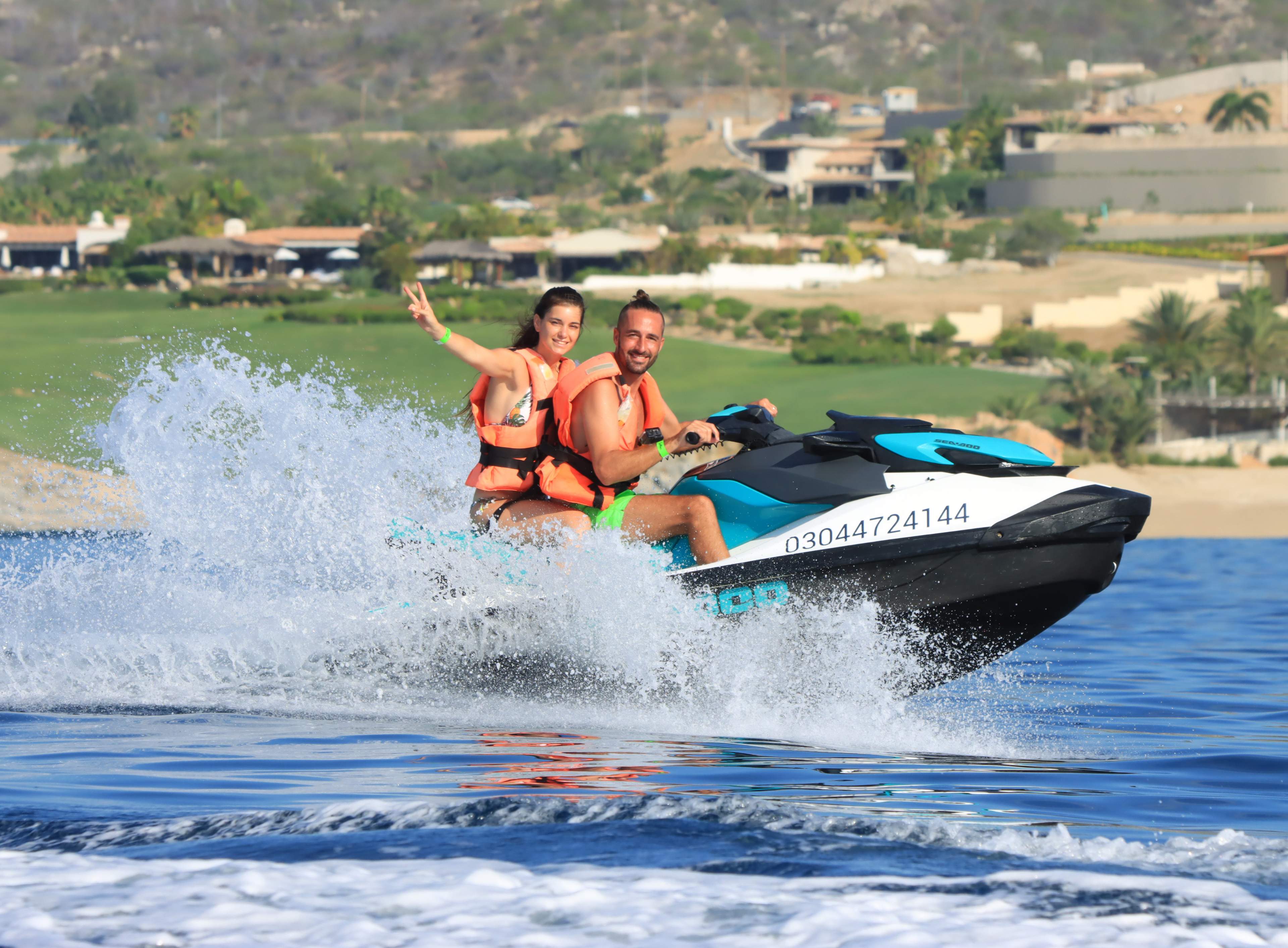Couple riding a jet ski with Cabo Adventures off the coast of Cabo, splashing through the waves.