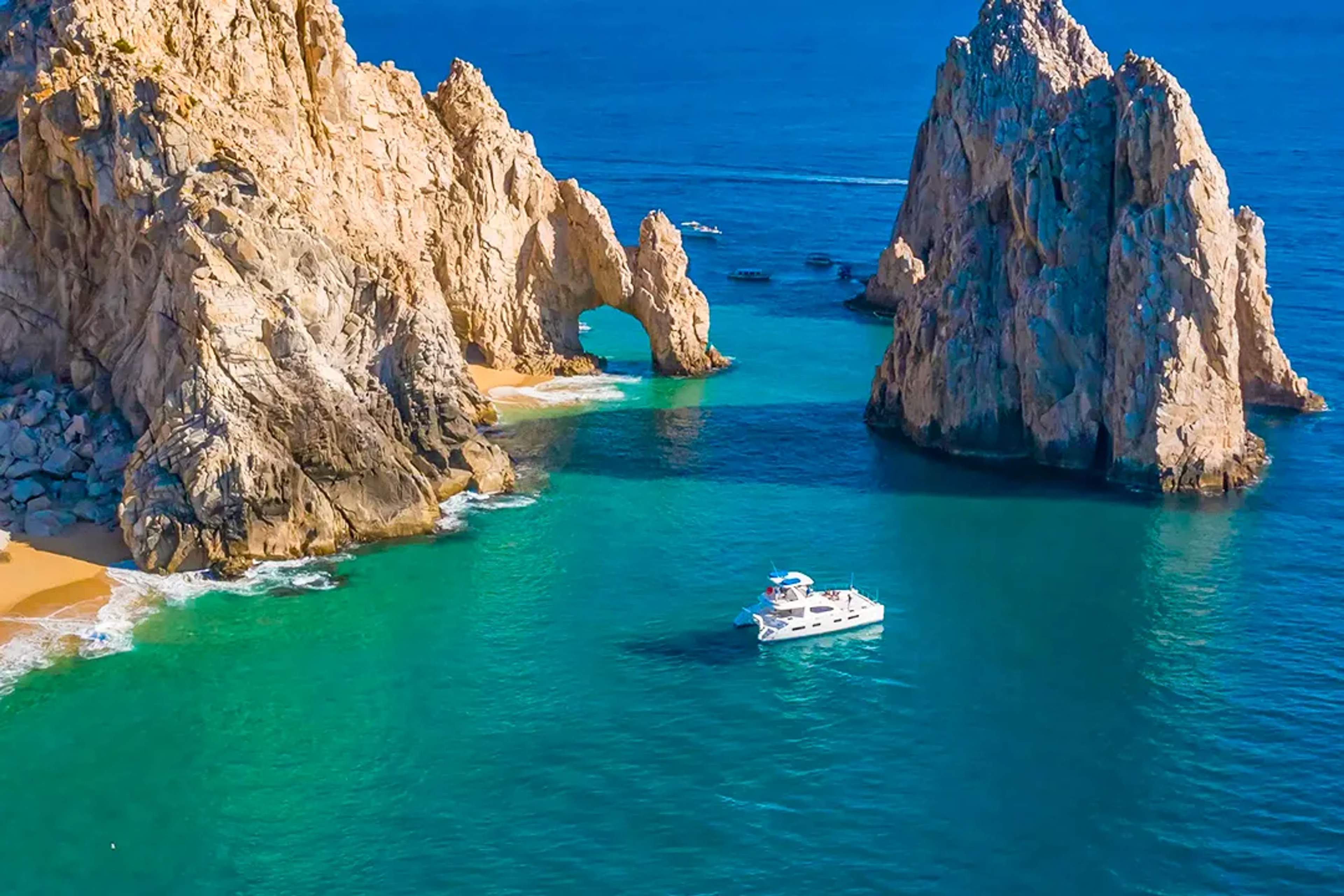 Luxury catamaran sailing near the Arch of Cabo San Lucas at Land’s End with turquoise water and rock formations