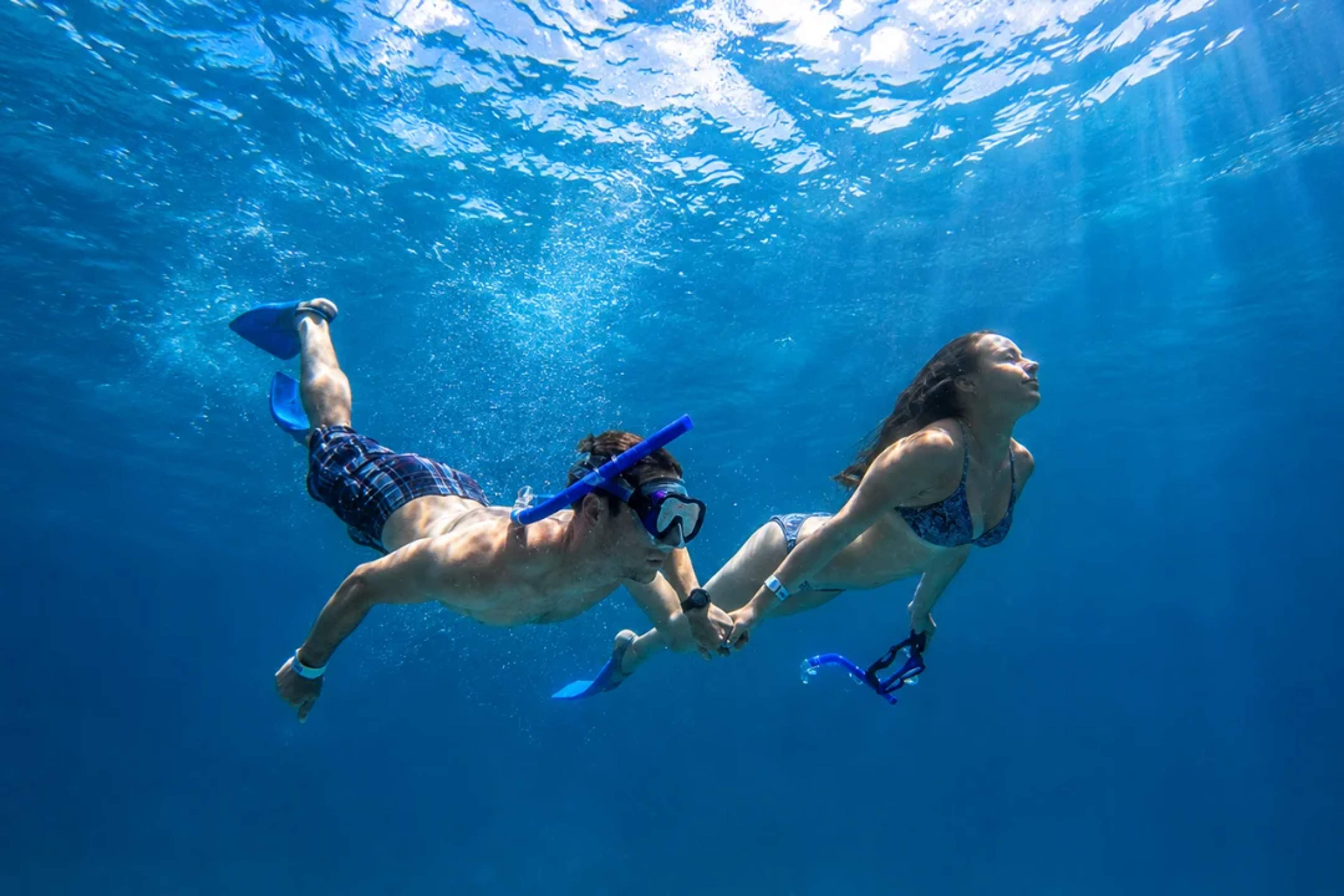 Couple snorkeling with sea scooters among coral reefs and tropical fish in clear blue water