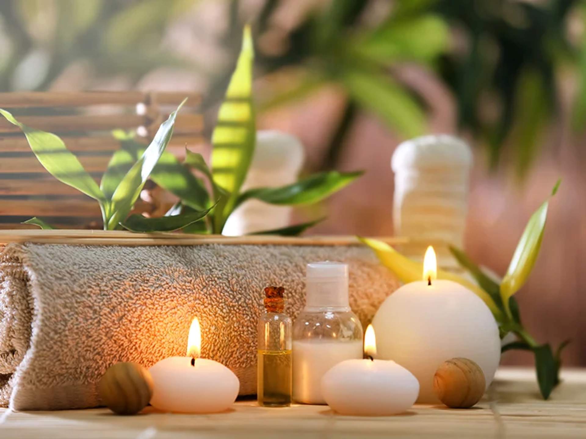 Ambiente de spa con velas encendidas, botellas de aceites esenciales, una toalla enrollada y hojas verdes, creando una atmósfera relajante.