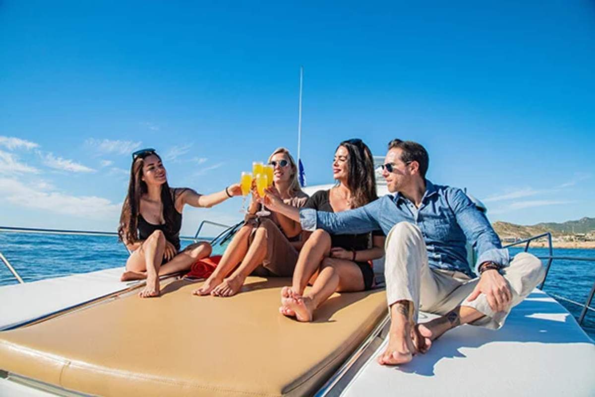 Four friends toasting with drinks on a yacht, enjoying a sunny day in Cabo.