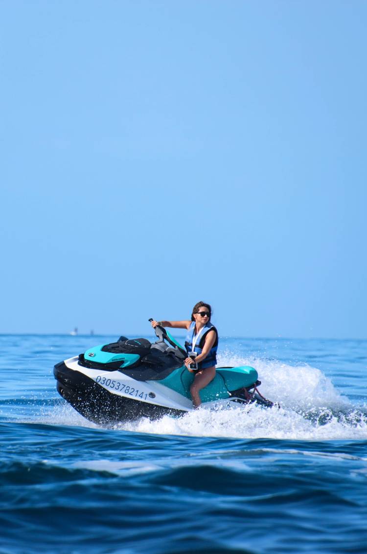 A woman rides a jet ski in the ocean, wearing sunglasses and a life jacket.