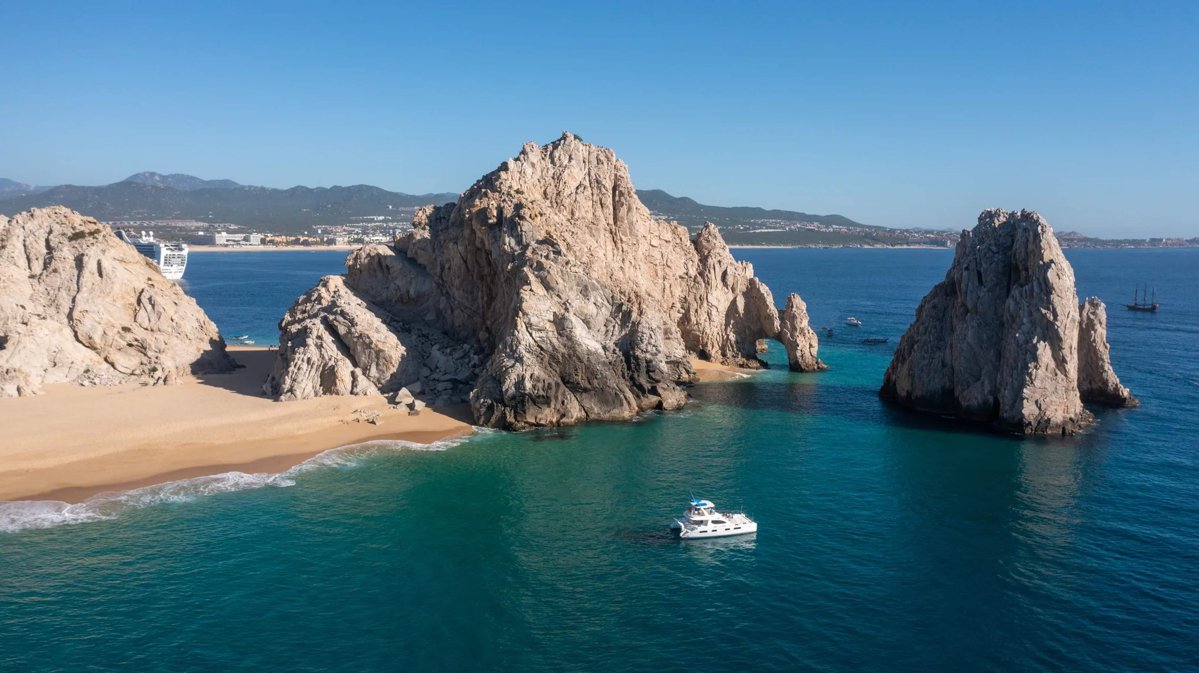 Promontorios rocosos dramáticos enmarcan una cala turquesa con un bote de snorkel anclado en aguas tranquilas y claras en