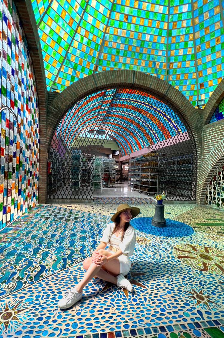 Mujer sentada en un suelo de mosaico colorido bajo una cúpula vibrante de vitrales.