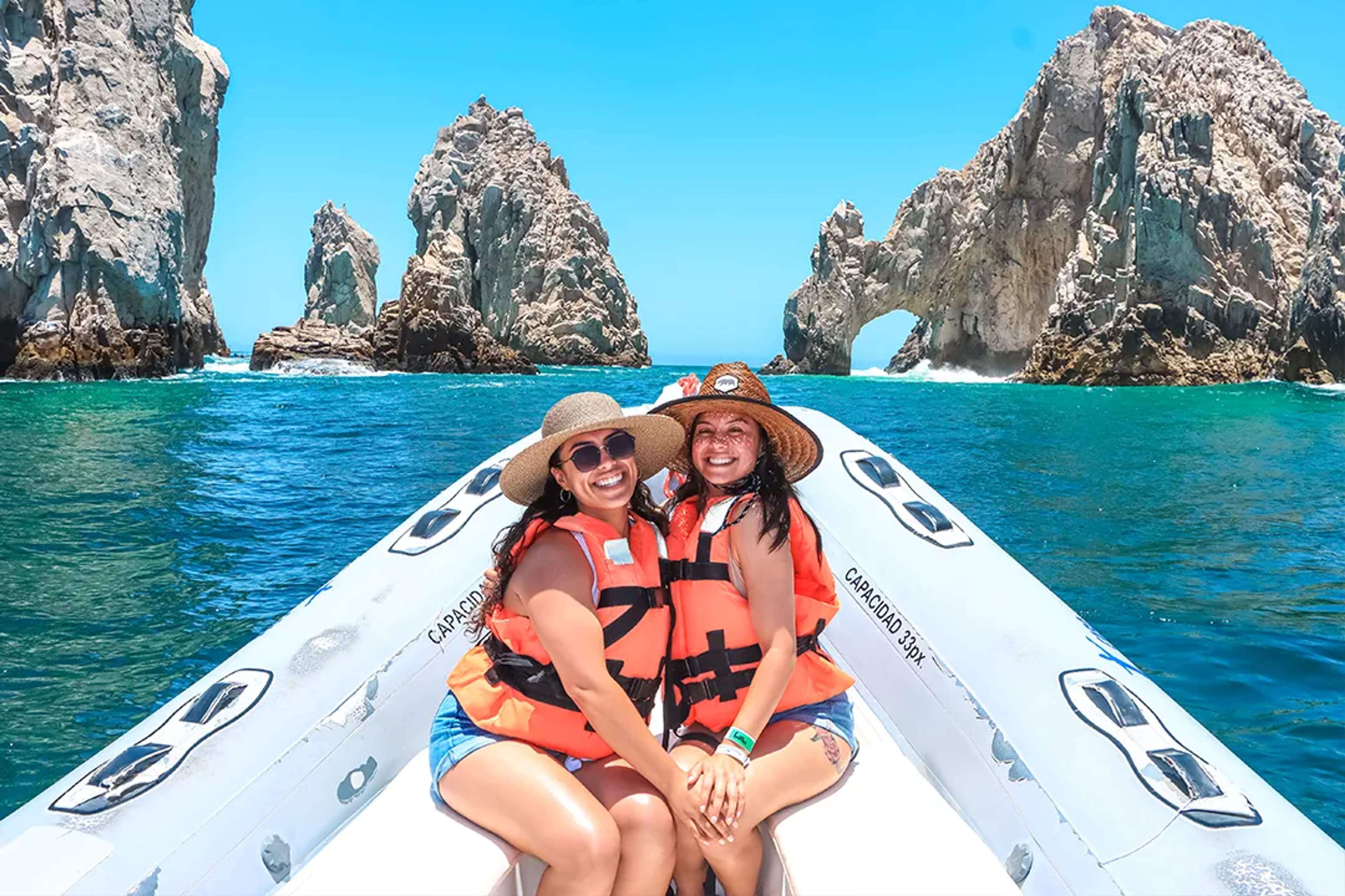 Two women enjoying a boat ride at El Arco in Cabo San Lucas, wearing life jackets with turquoise sea views