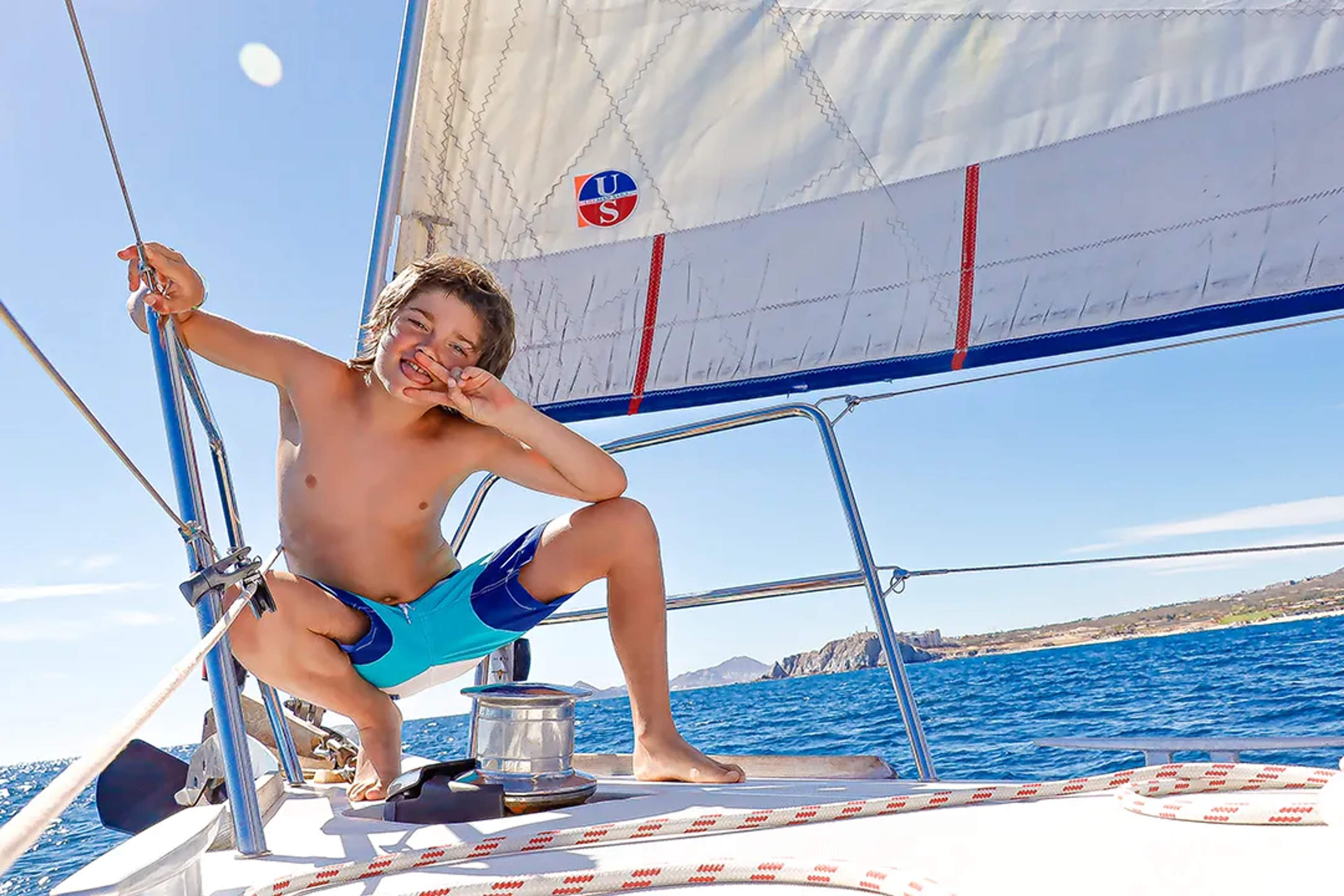 Happy boy makes a peace sign while sailing on a boat under the sun and blue sky.