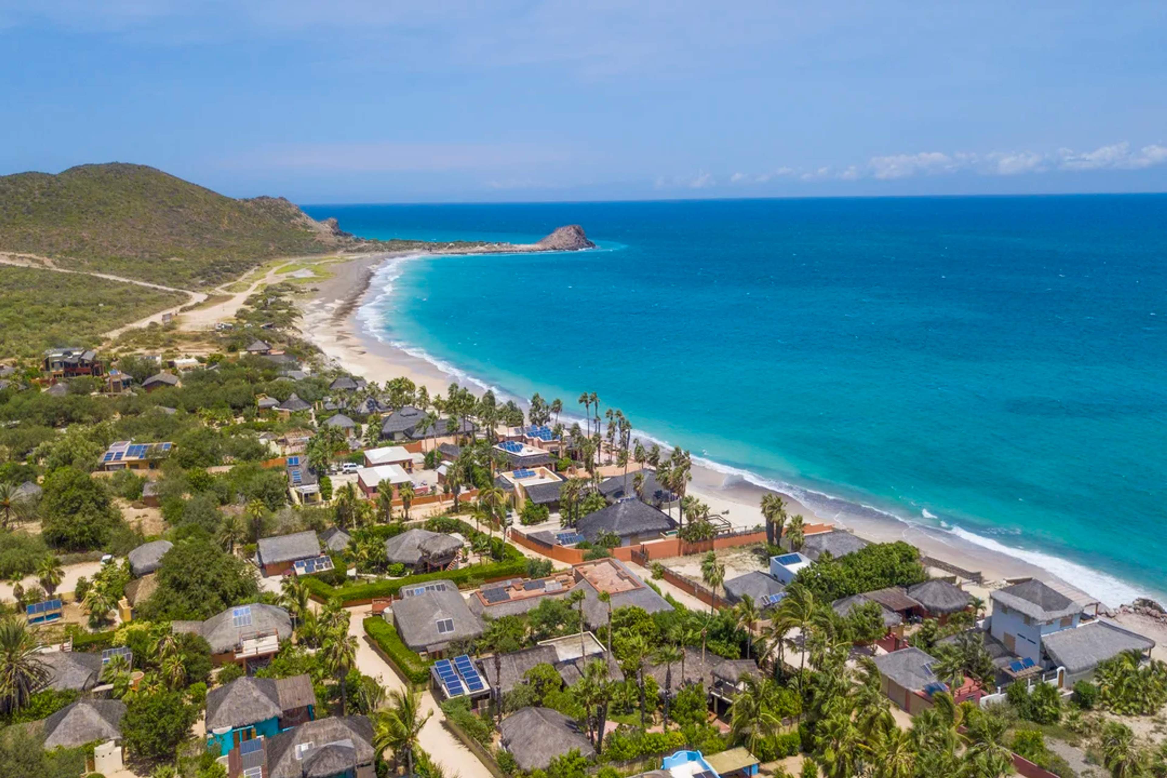 Aerial view of Cabo Pulmo's coastline with houses, lush greenery, and the blue ocean, showcasing its natural beauty and serene environment.