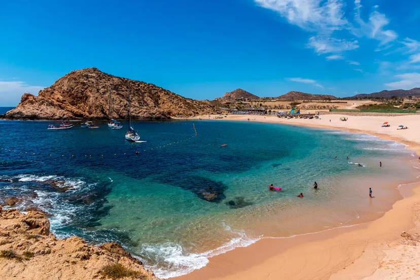 Calm turquoise bay with anchored boats and swimmers enjoying a sunny day at Chileno Beach, Cabo.