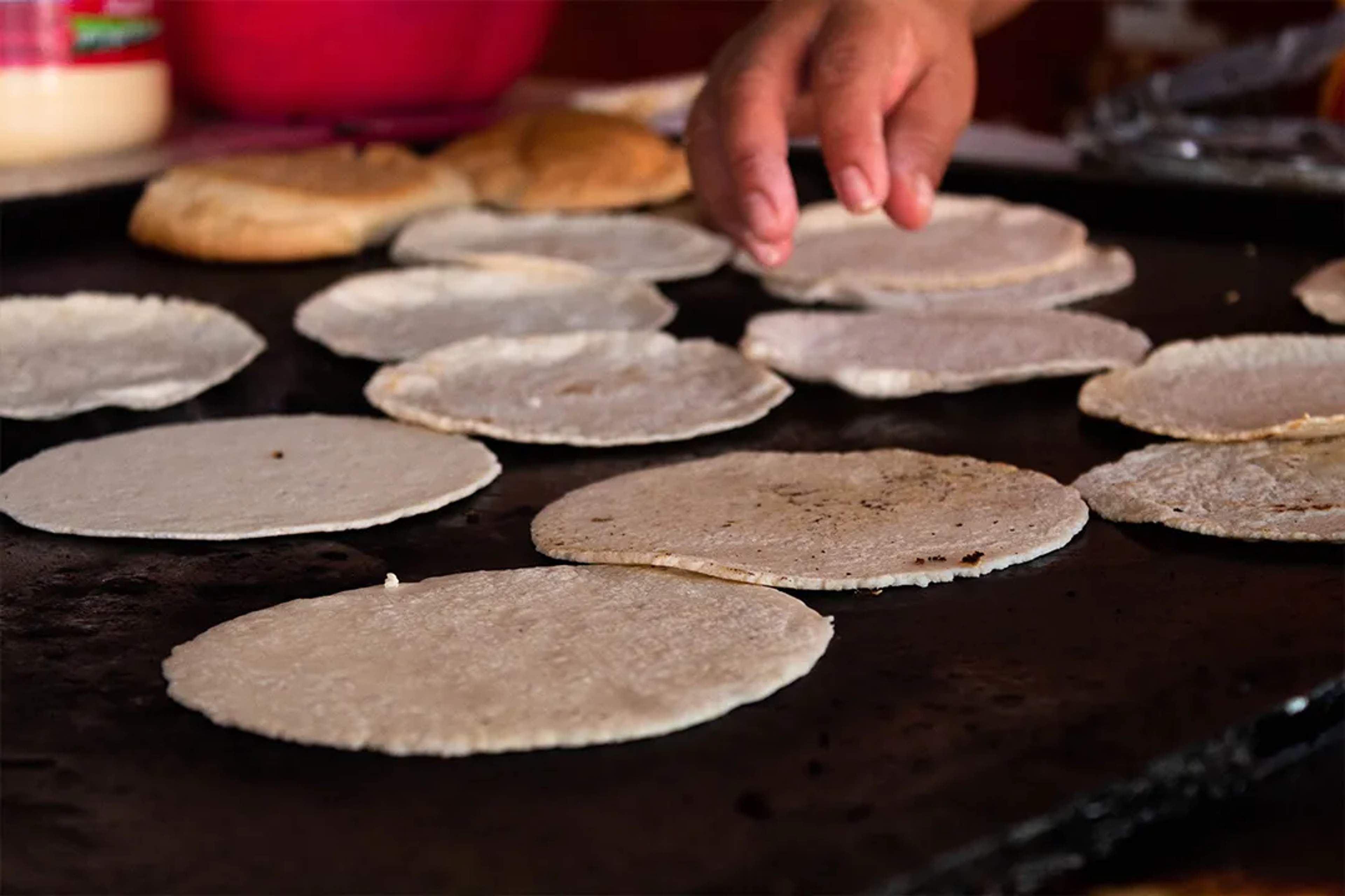 Hand making fresh corn tortillas on a traditional comal during Mexican cooking experience in Los Cabos