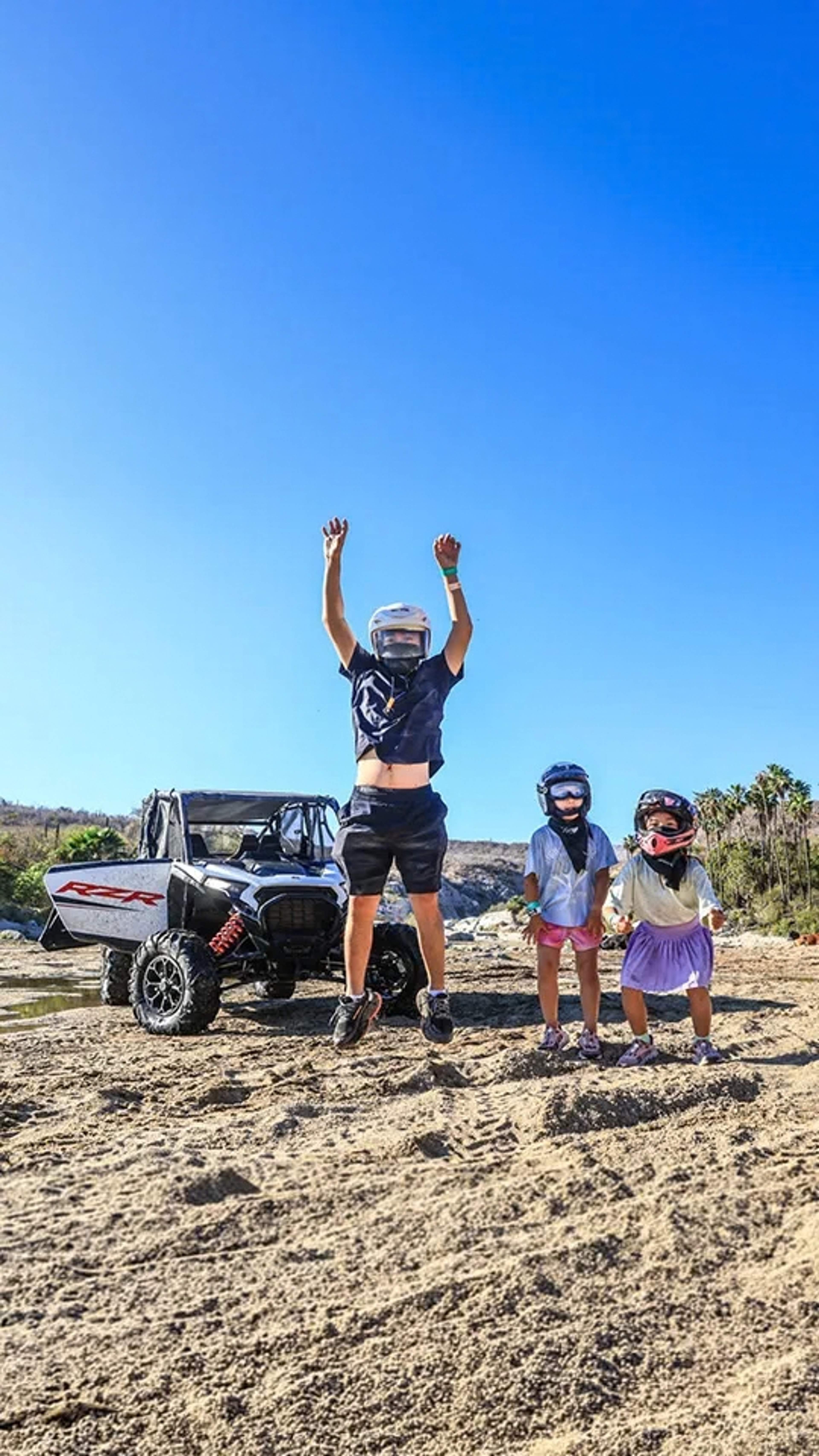 Family with kids jumping beside a UTV during a Cabo Adventures desert tour in Los Cabos.