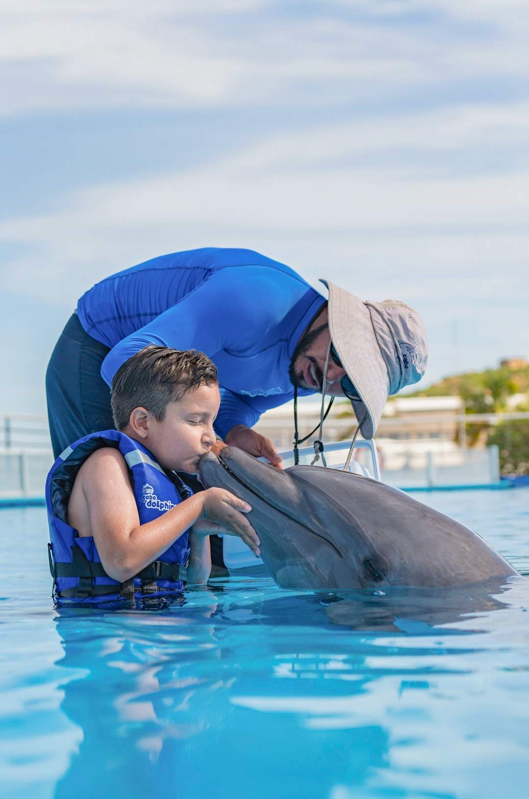 Niño besando un delfín durante un tour de nado con delfines en Cabo San Lucas.