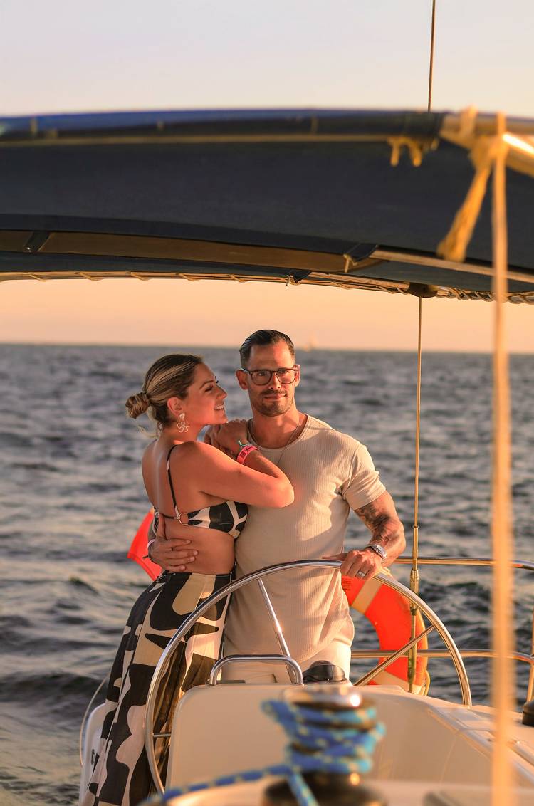 A couple embraces at the helm of a sailboat, enjoying a romantic sunset cruise on the open sea.