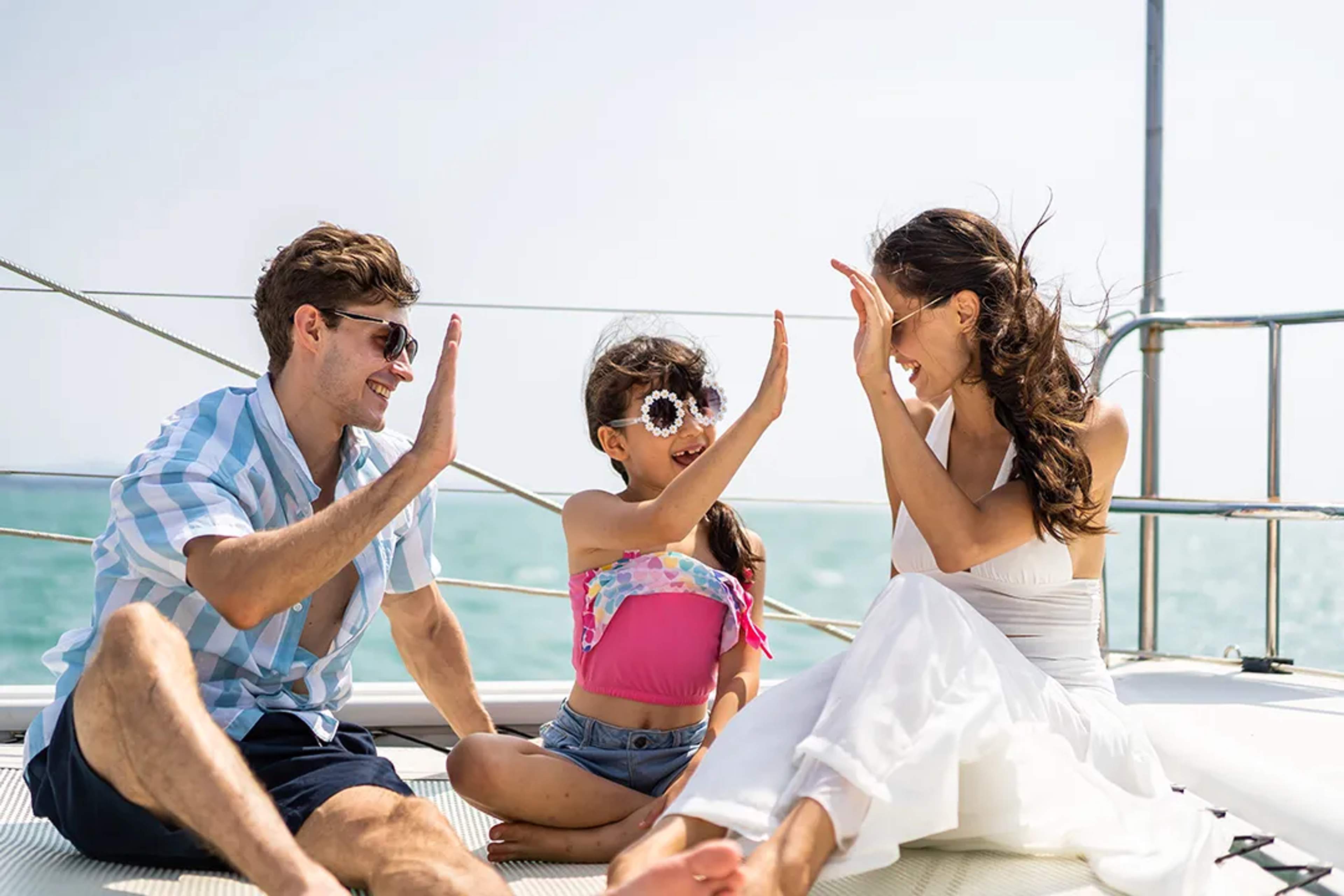Smiling family shares high fives while enjoying a sunny yacht ride together.
