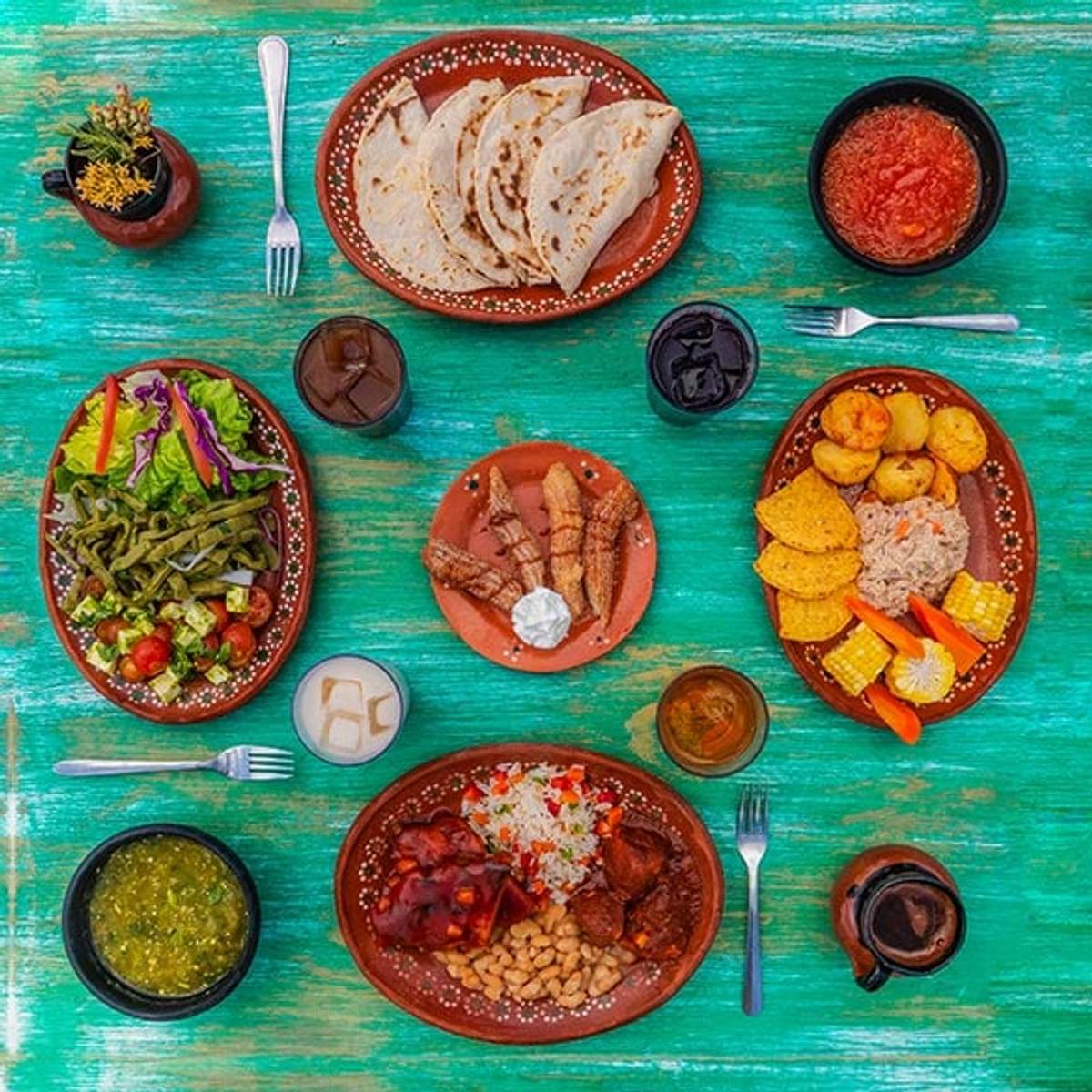 An overhead view of a colorful Mexican meal spread on a rustic green table, featuring salads, tortillas, salsas, and various traditional dishes.