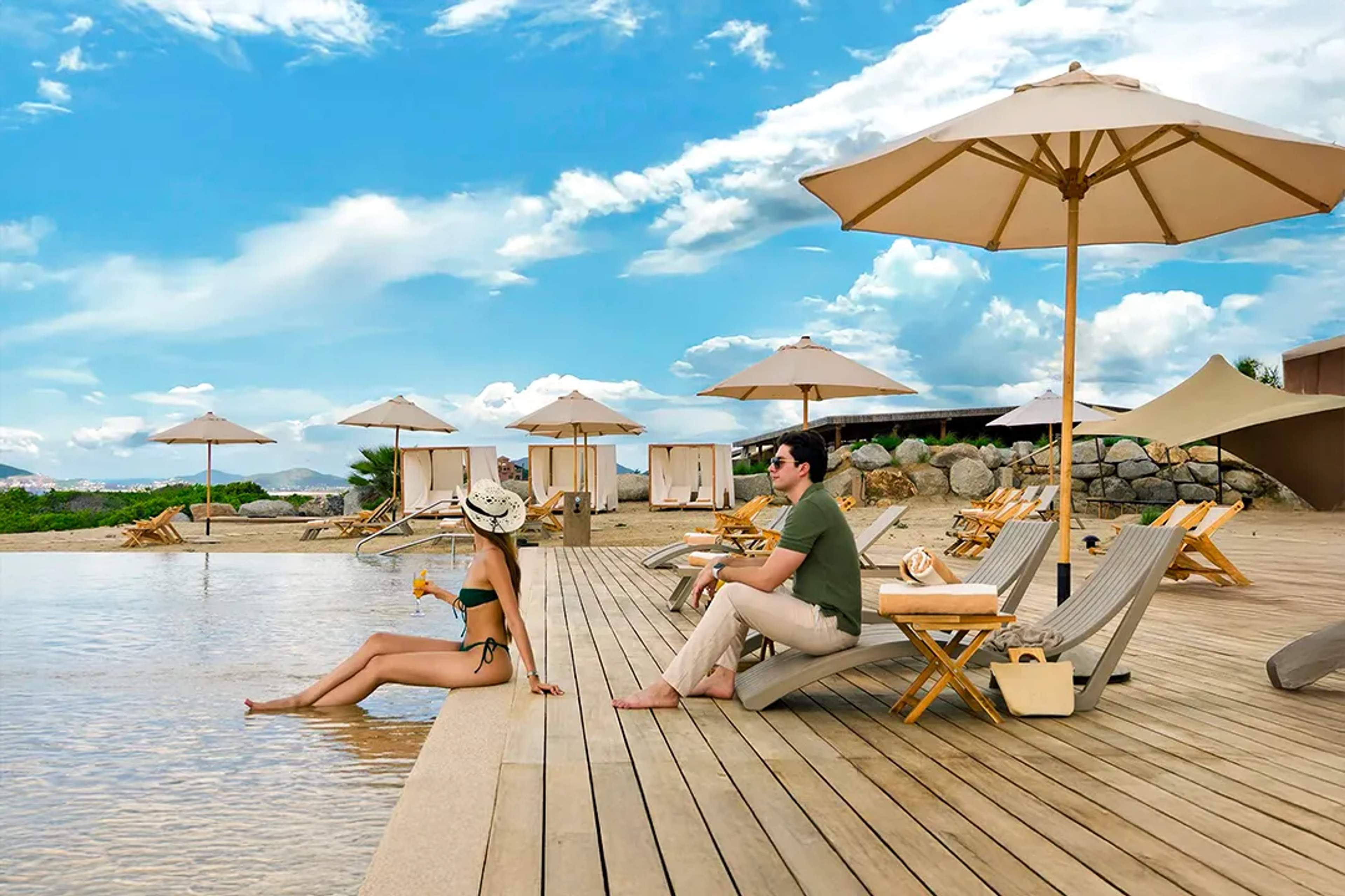 Luxury couple relaxing by an infinity pool with cabanas and ocean views at a beachfront resort in Los