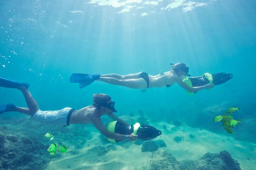 Couple snorkeling with sea scooters among coral reefs and tropical fish in clear blue water